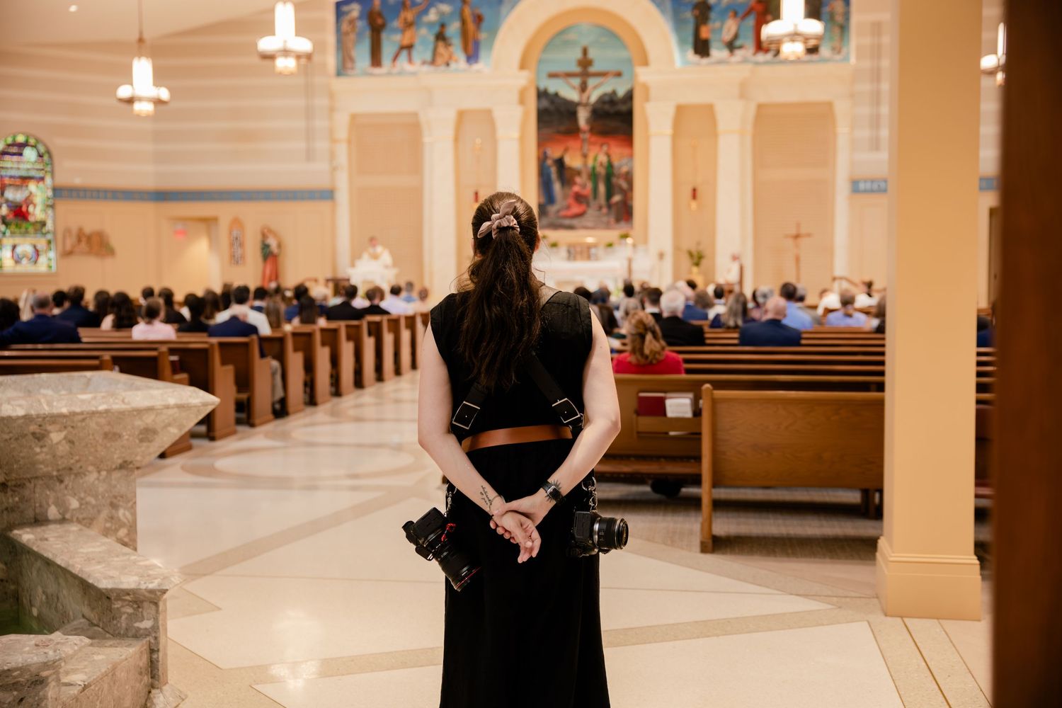 A photographer in a black dress stands at the back of a church sanctuary while attendees sit in wooden pews.
