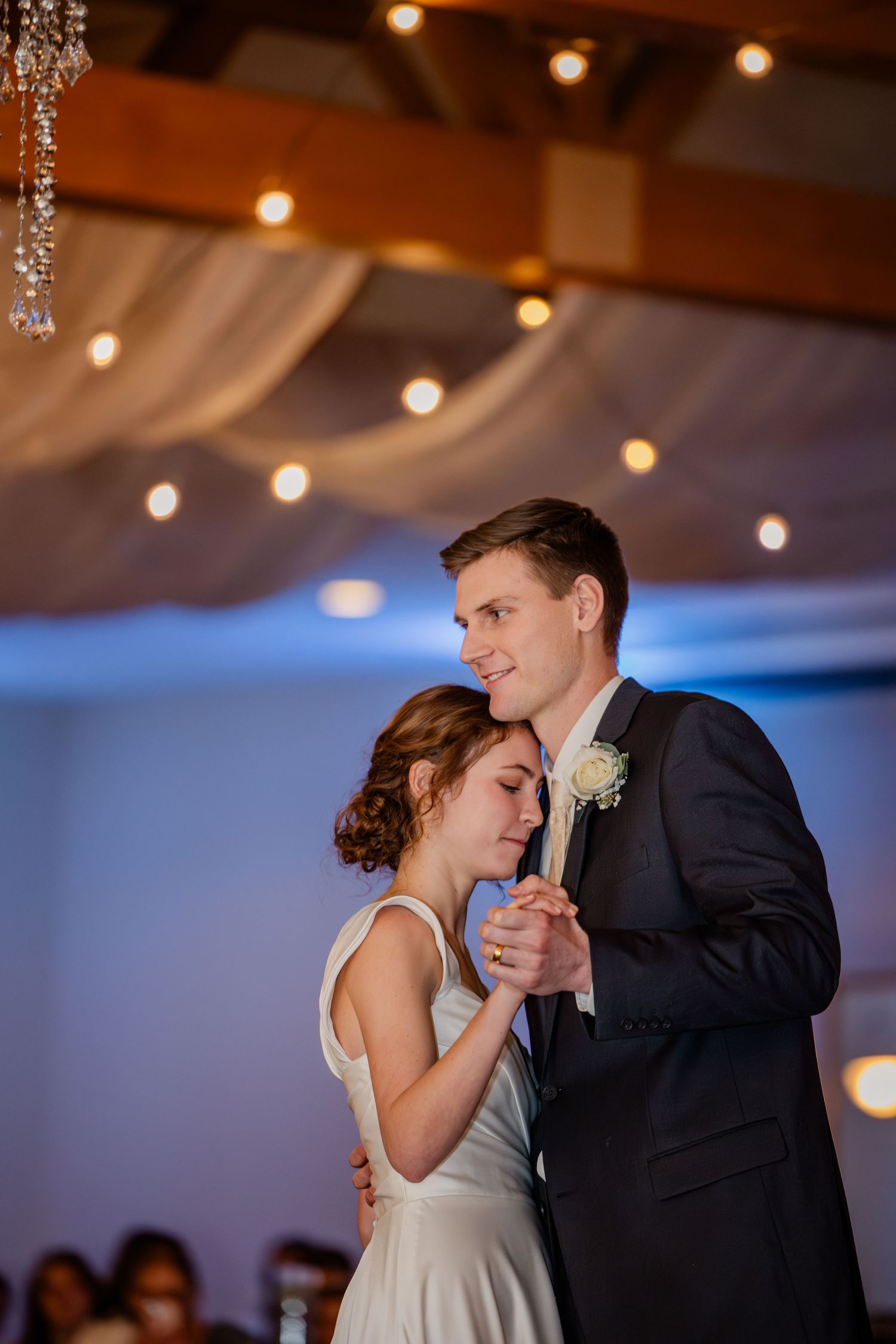 Bride and groom share their first dance under warm string lights and draped fabric at elegant wedding reception.
