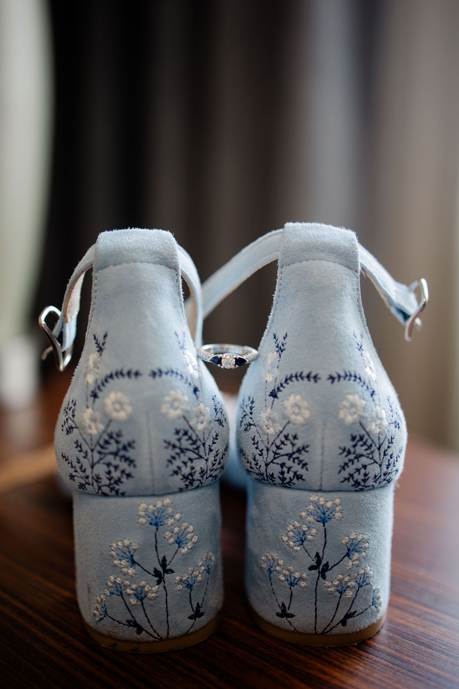 Wedding heels in pale blue with delicate floral and snowflake embroidery details shown from behind on wooden surface.