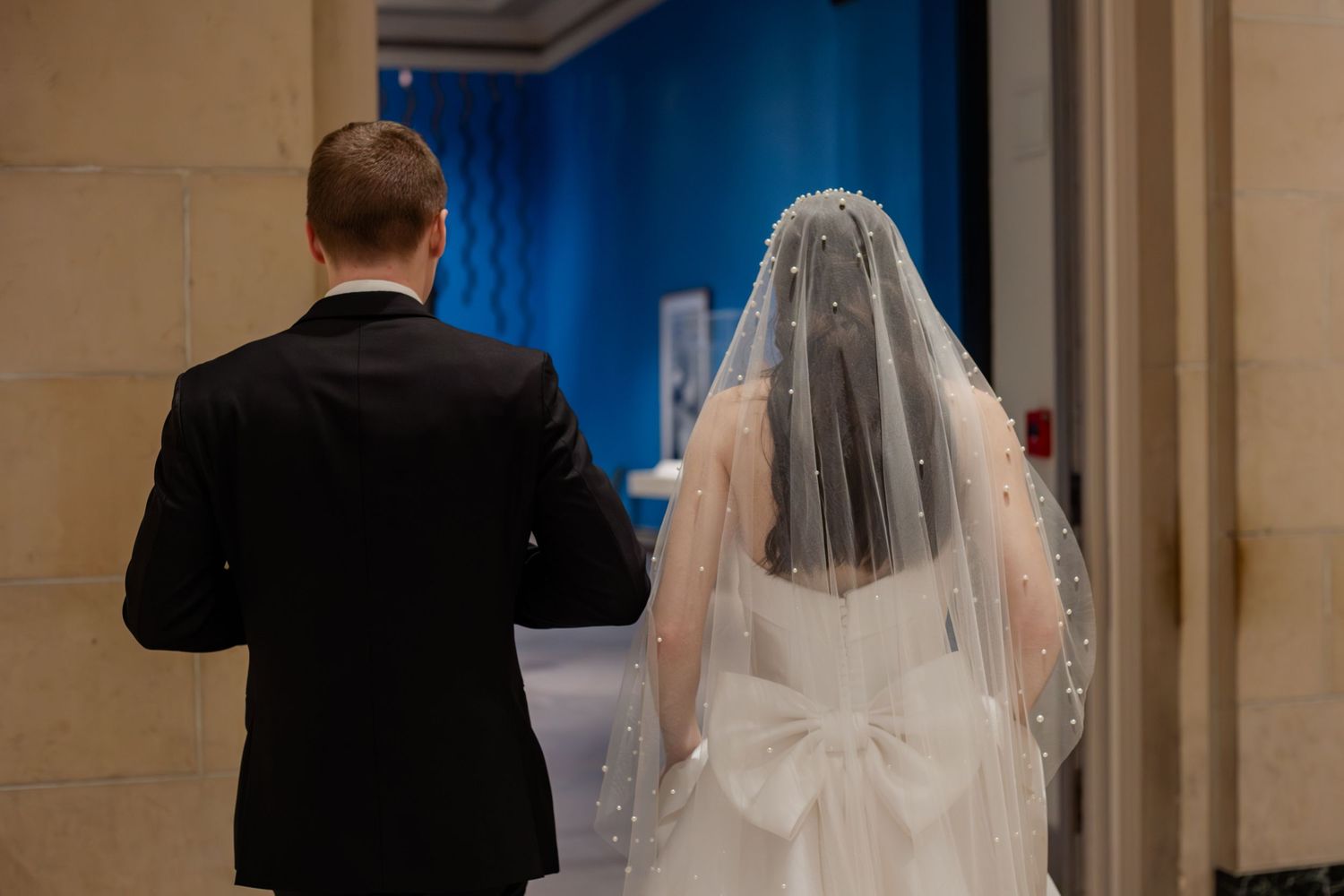 Bride in white gown with veil and groom in black suit walking together at wedding ceremony.