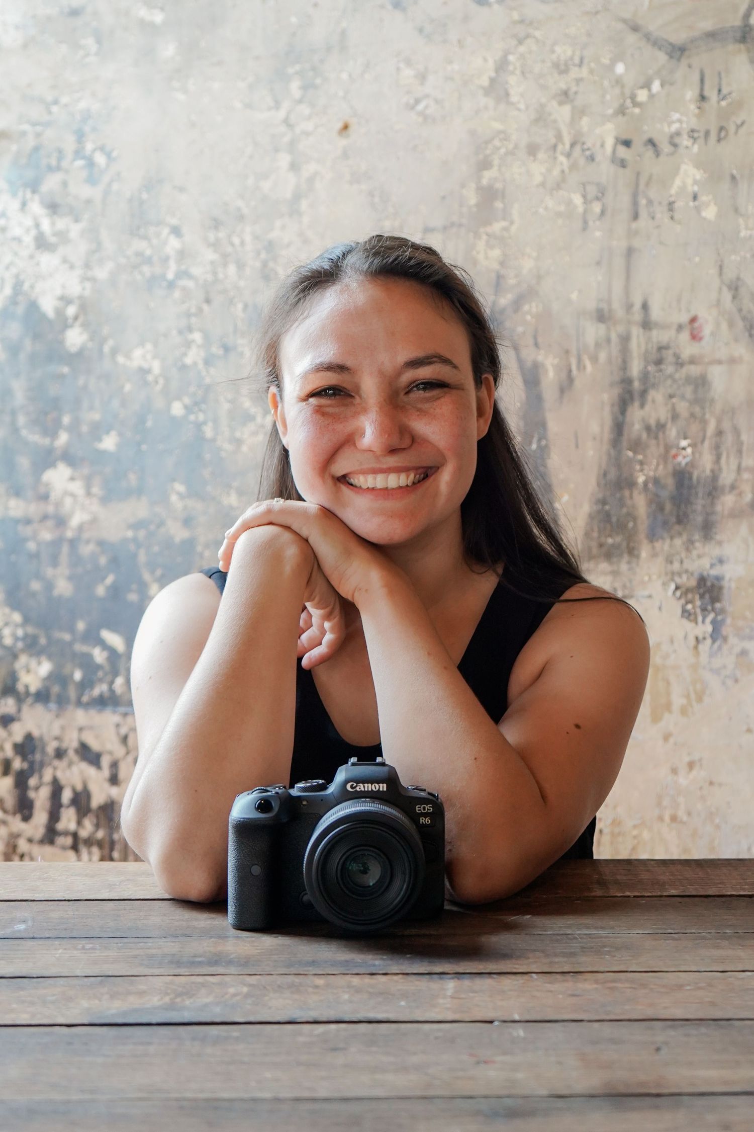 Professional photographer rests on wooden table with DSLR camera while taking portraits in rustic setting.
