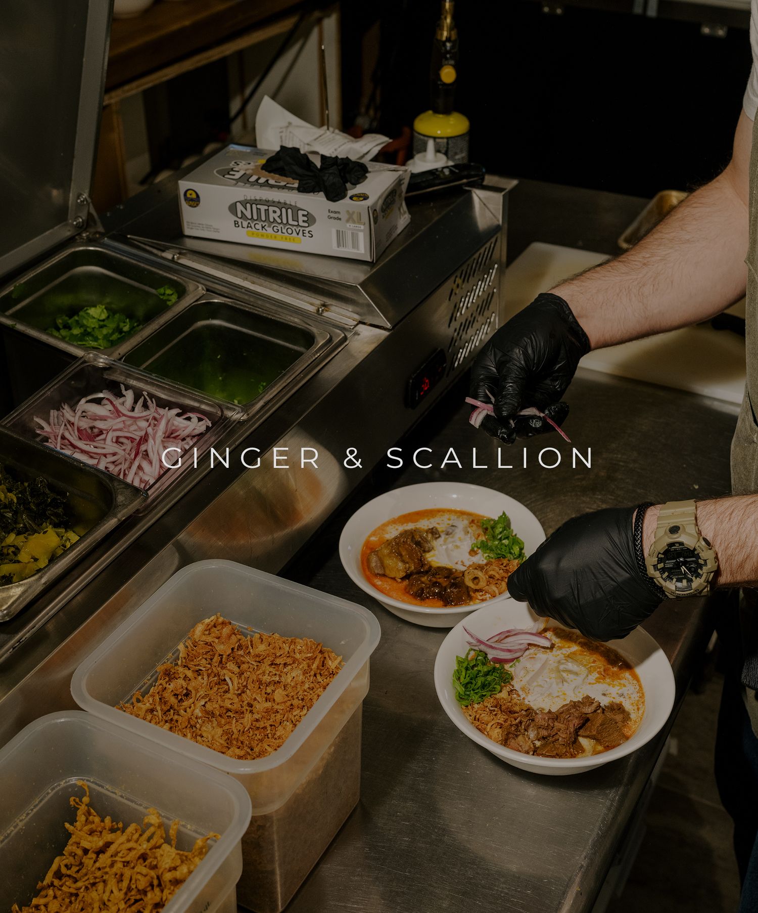 Restaurant kitchen staff in black gloves preparing Asian dishes with noodles and toppings at food service station.