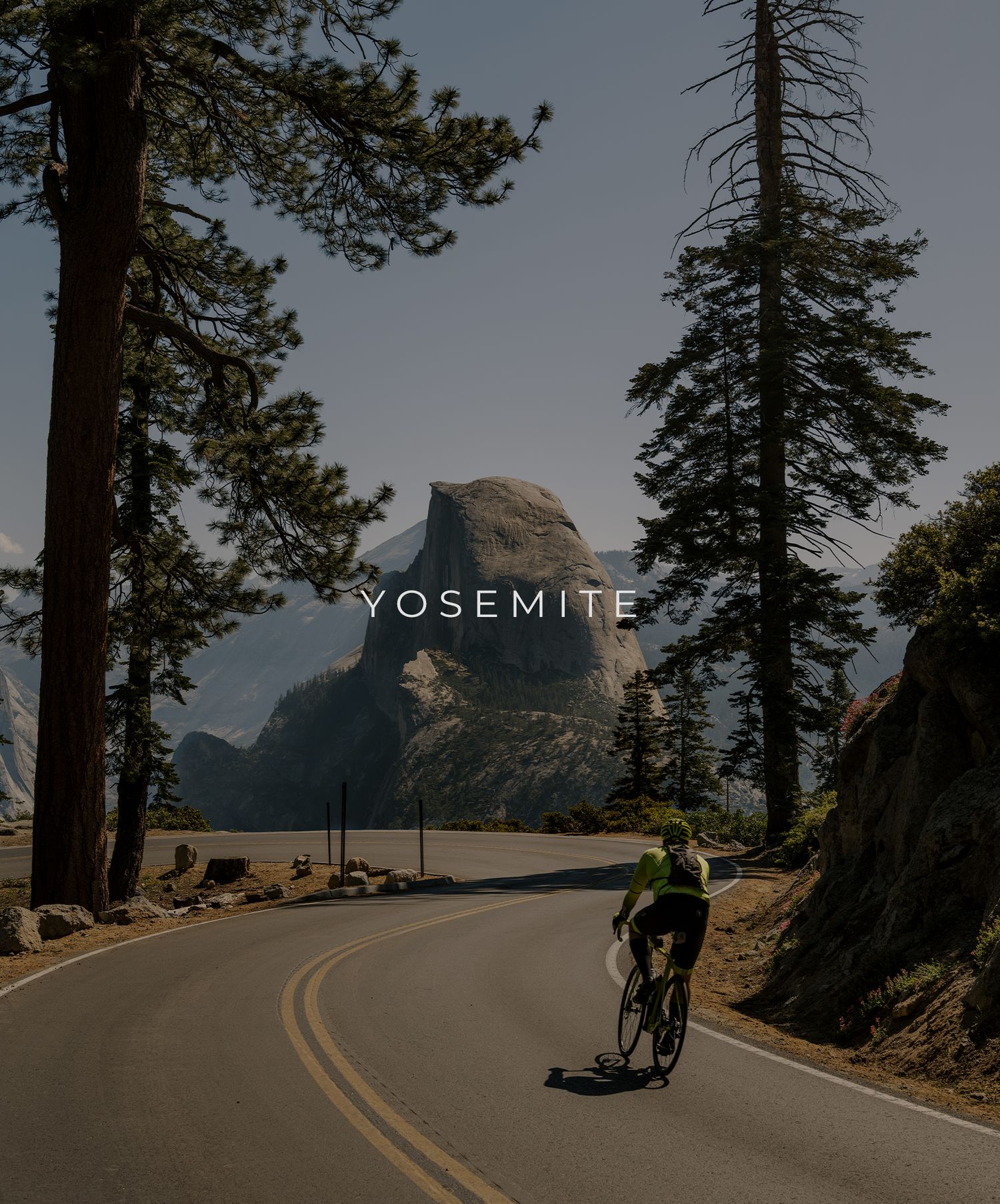 Cyclist rides along curved mountain road with iconic Half Dome rock formation in Yosemite National Park.