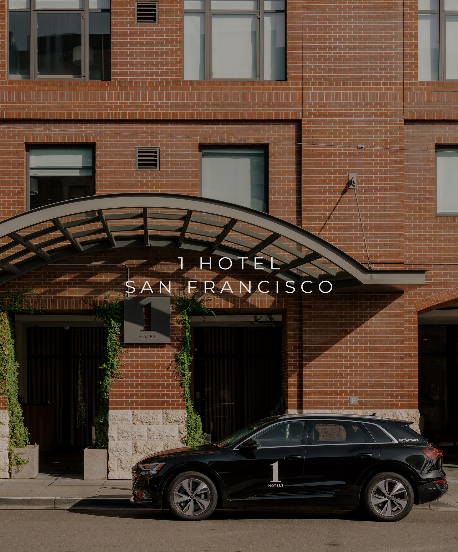 A black luxury SUV is parked in front of the 1 Hotel San Francisco entrance with its brick facade and curved awning.