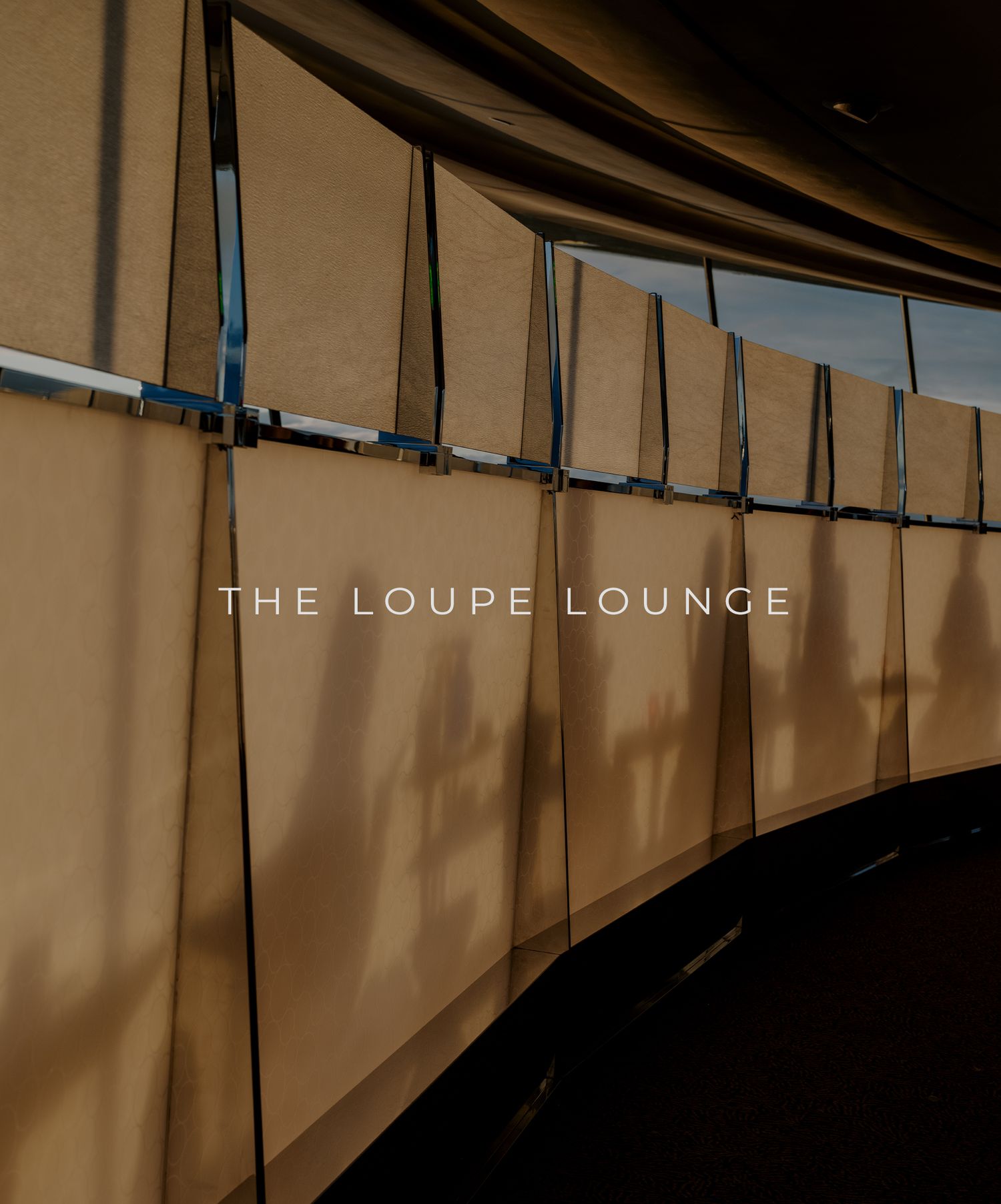 Curved wall with hanging beige curtains and black metal fixtures displaying 'THE LOUPE LOUNGE' text in modern lettering.