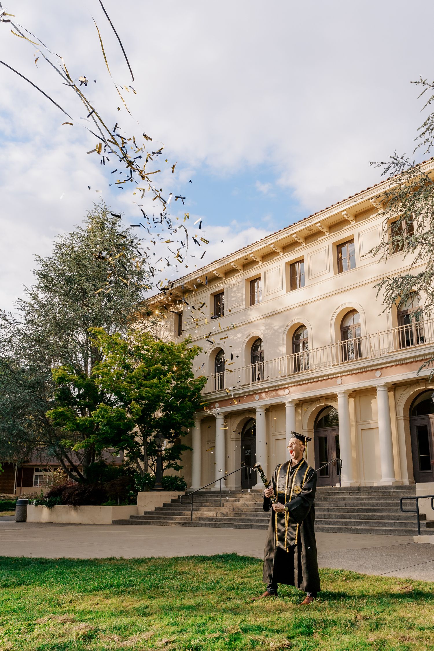 Graduate stands in front of historic academic building with classical architecture.