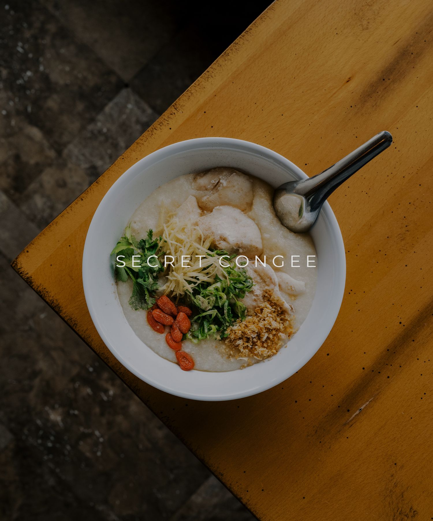 Overhead view of a rice congee bowl topped with broccoli, carrots and garnishes on a wooden surface.