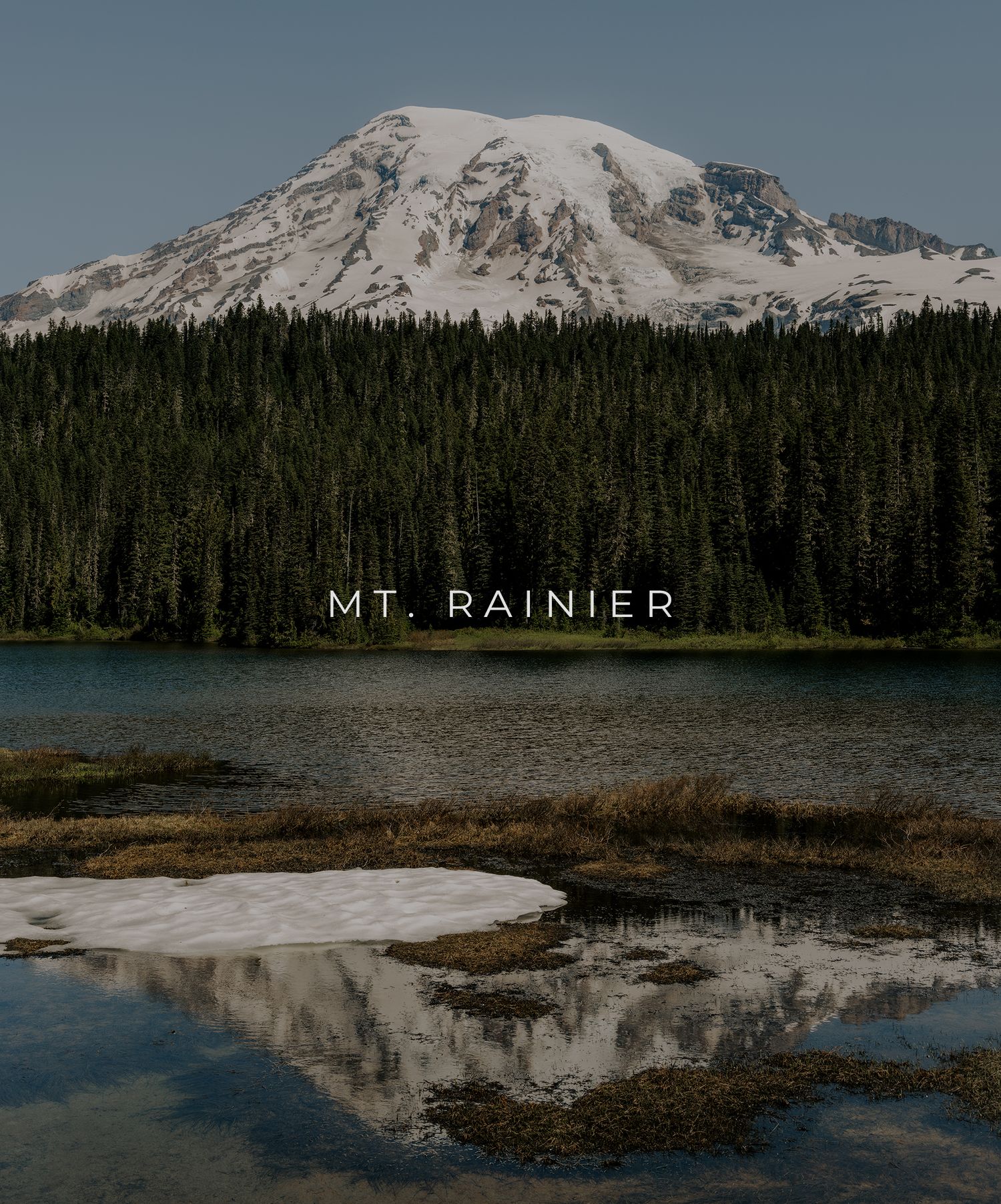 Snow-capped Mount Rainier towers over a pristine Reflection Lake surrounded by dense evergreen forest in Washington state.