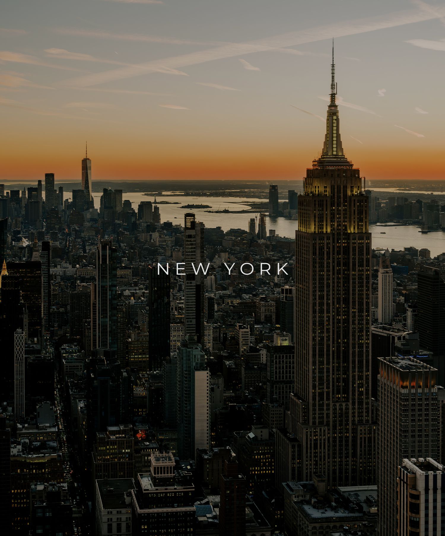 Aerial view of New York City skyline at sunset featuring Empire State Building and urban landscape against orange sky.
