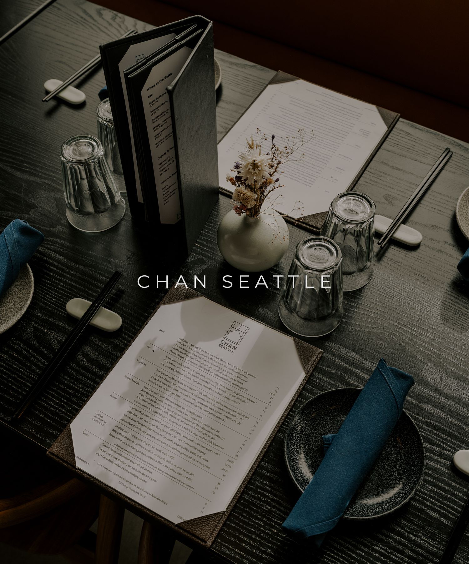 Restaurant table setting at Chan Seattle with menu, glasses and place settings in moody lighting.
