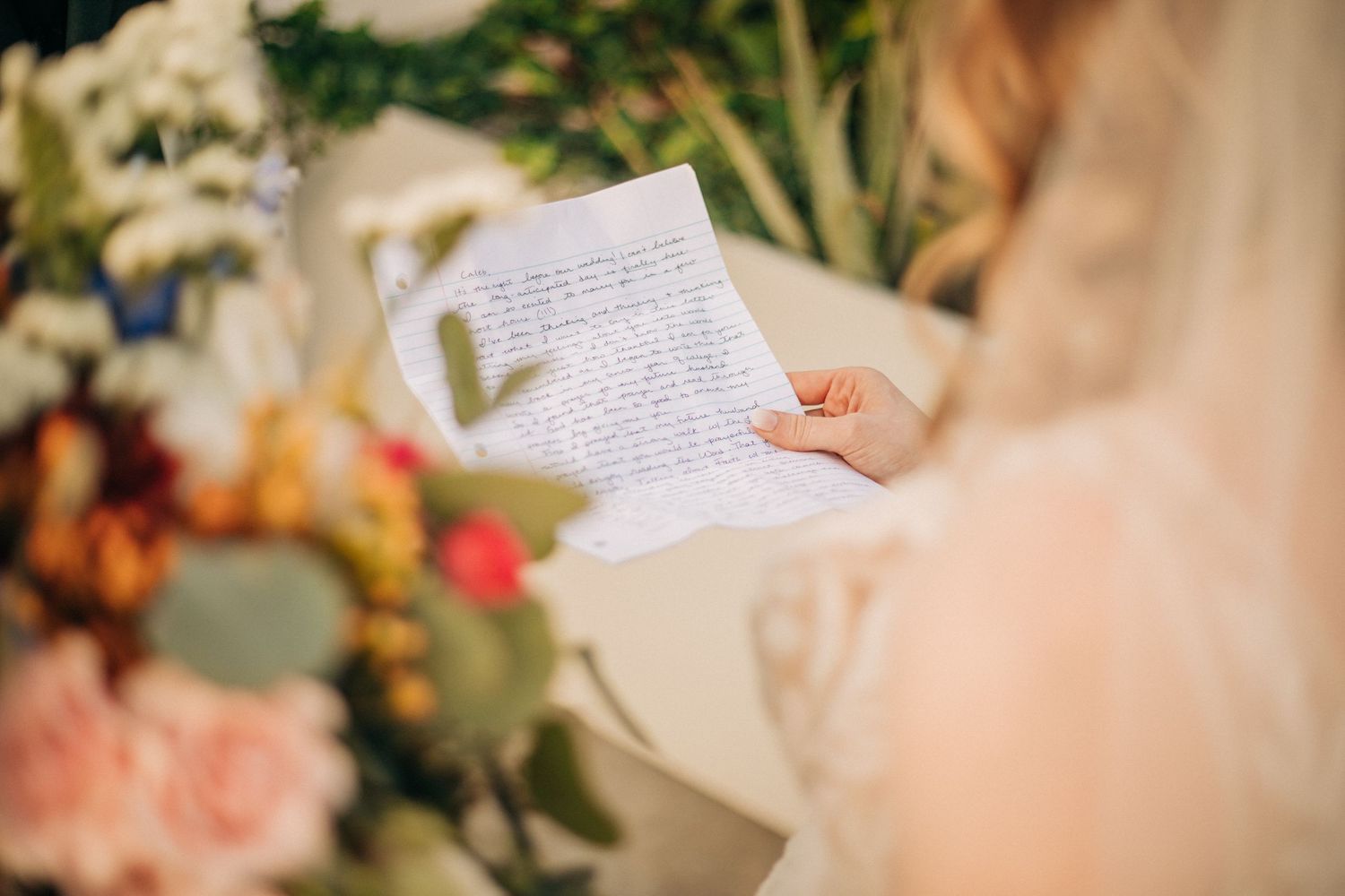 Someone holds and reads a handwritten letter while standing next to colorful floral arrangements.