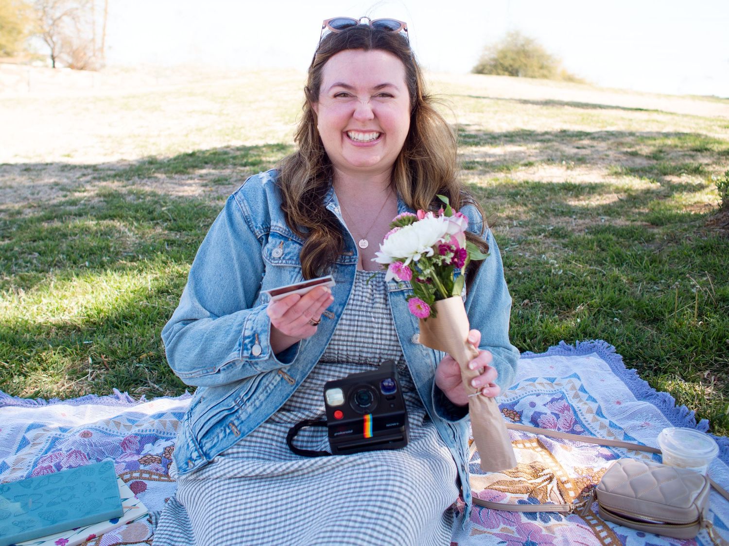 Kelsey enjoying a picnic outdoors on a blanket with flowers and snacks on a sunny day.