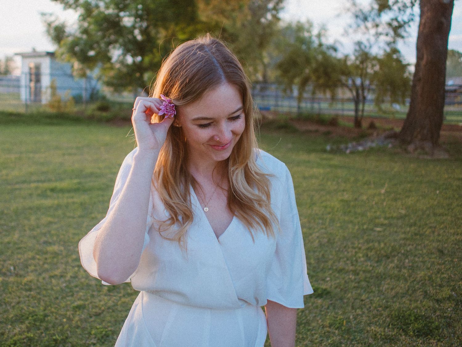 Young woman wearing a white dress smiles while playing with a pink flower in her hair at blue hour.