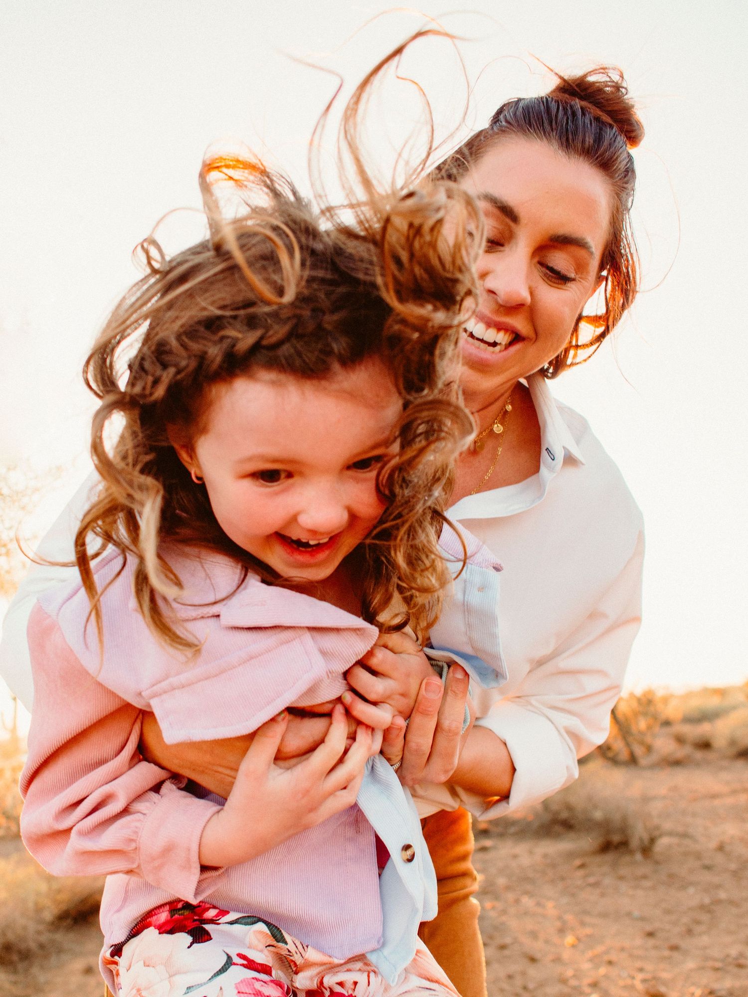 A joyful candid moment captured at sunset shows playful interaction and genuine laughter between mom and daughter.