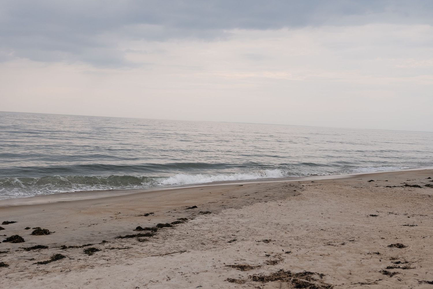 Overcast beach landscape with waves gently rolling onto sandy shore.