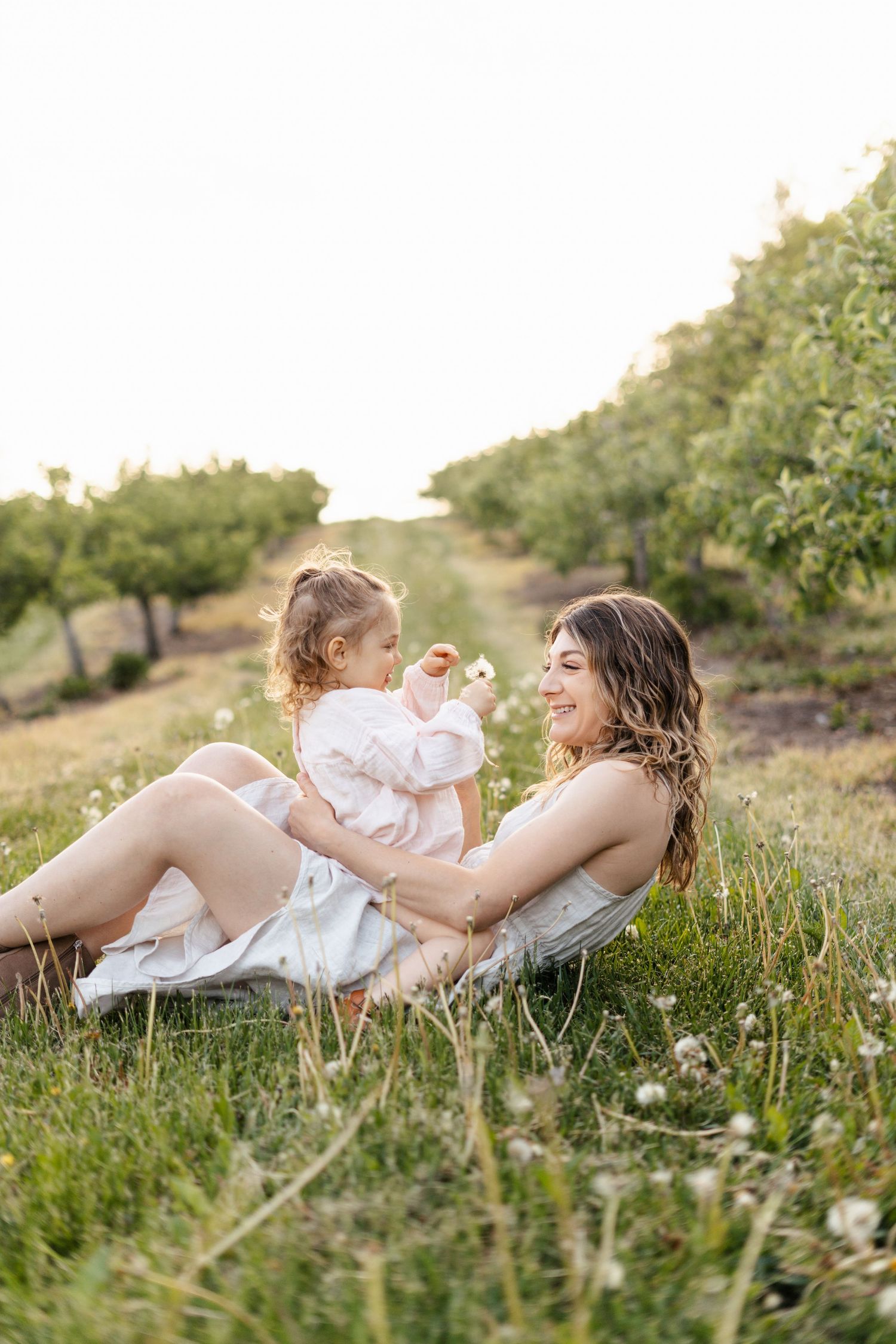 Mother and child lying in a sunlit meadow during golden hour photo session.