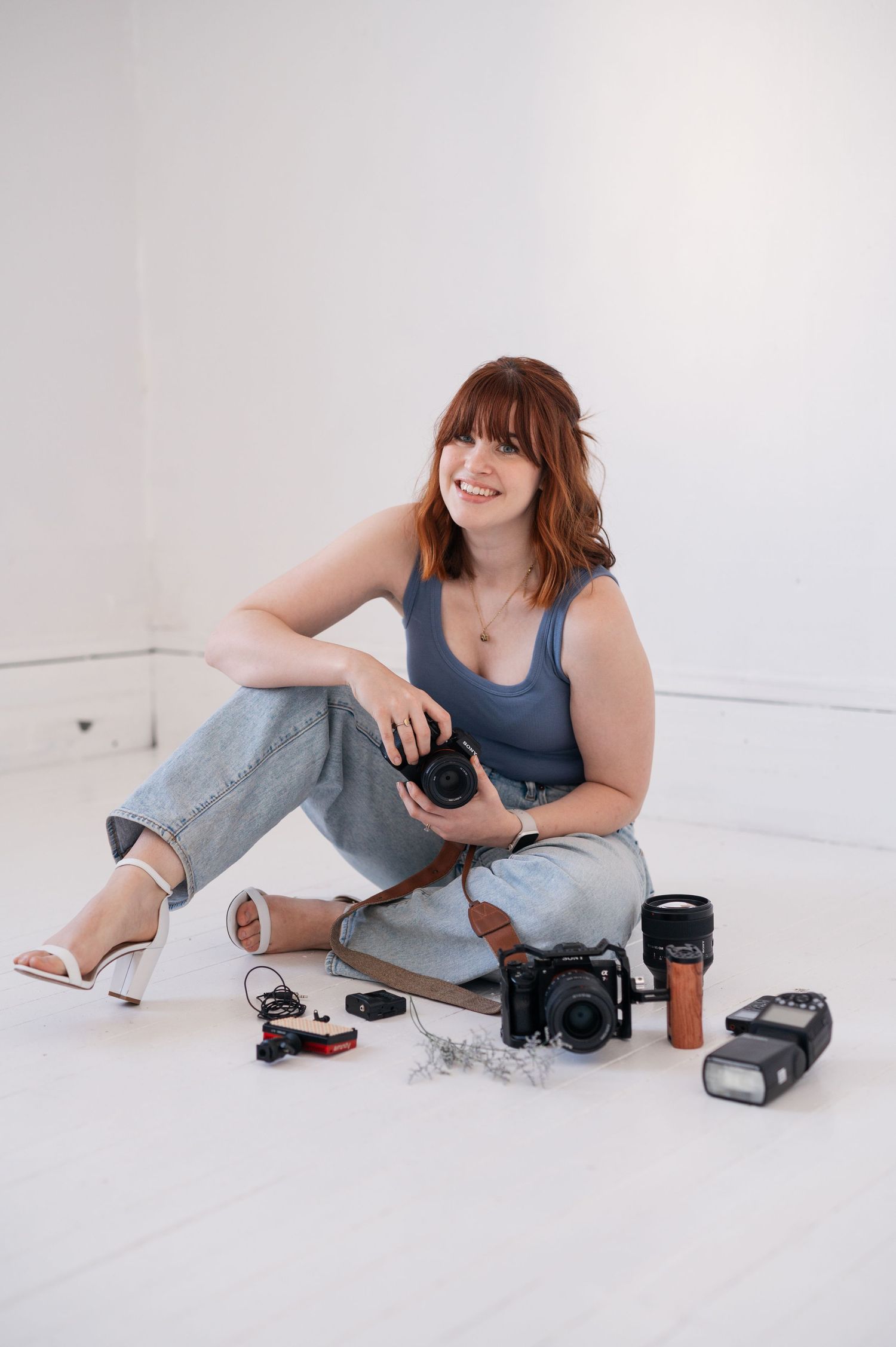 Photographer with camera gear arranged on white studio floor.