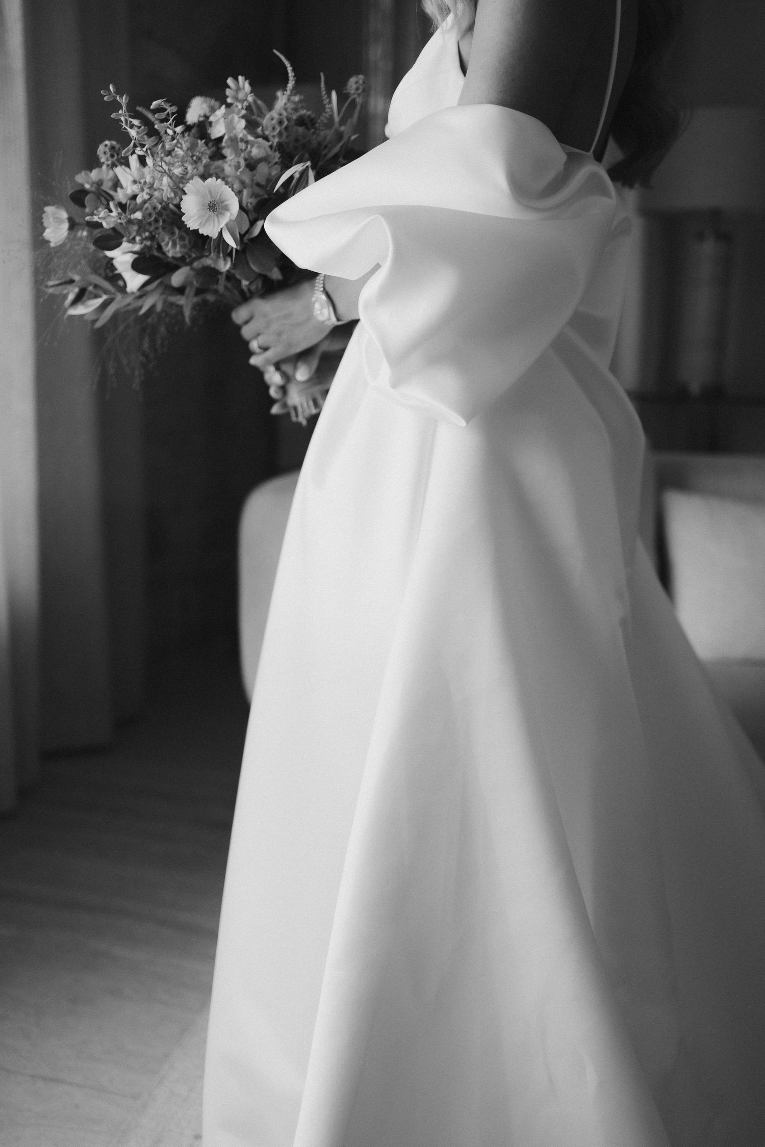 Elegant white wedding dress detail showing flowing fabric and texture in black and white.