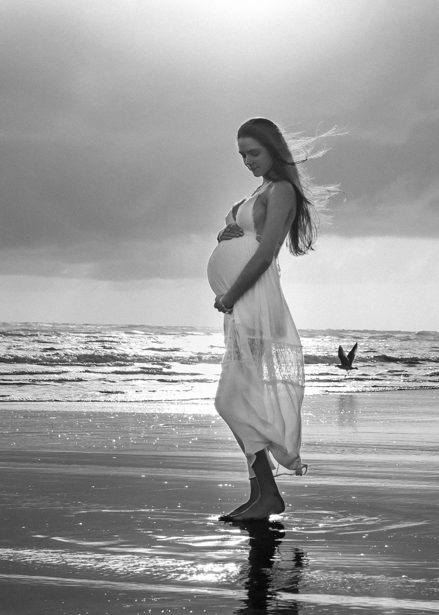 Pregnant mother embracing her belly for a Maternity photoshoot at sunset on a west Auckland beach. CL Photography. Piha. Golden hour