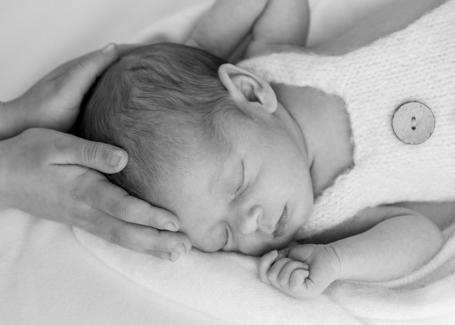 Soft black and white image of newborn. Big sisters hands are holding baby's head. Newborn photoshoot