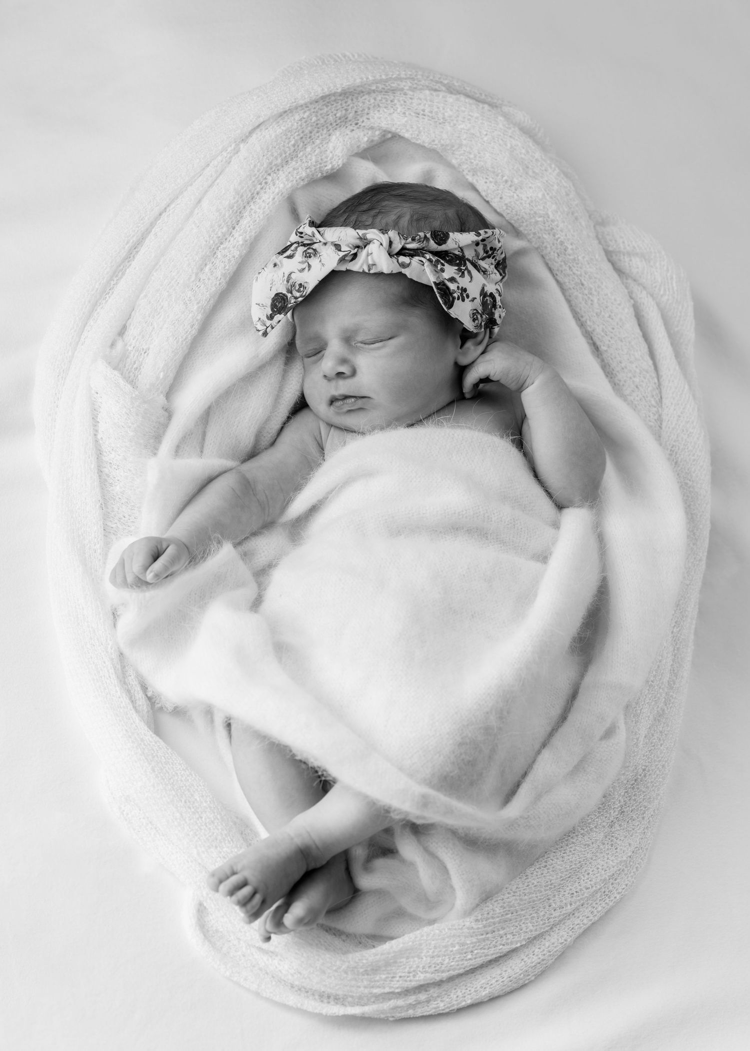 Newborn baby sleeping - wrapped in white wooden blanket, with textured knits. Floral headband, legs crossed. Newborn photography.