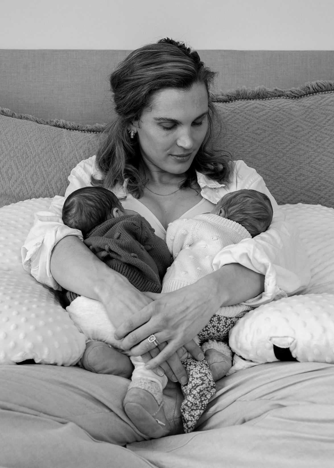 Mother sitting on her bed breastfeeding twin babies. Neutral colours. Newborn lifestyle photoshoot. Catherine Lundin Photography.