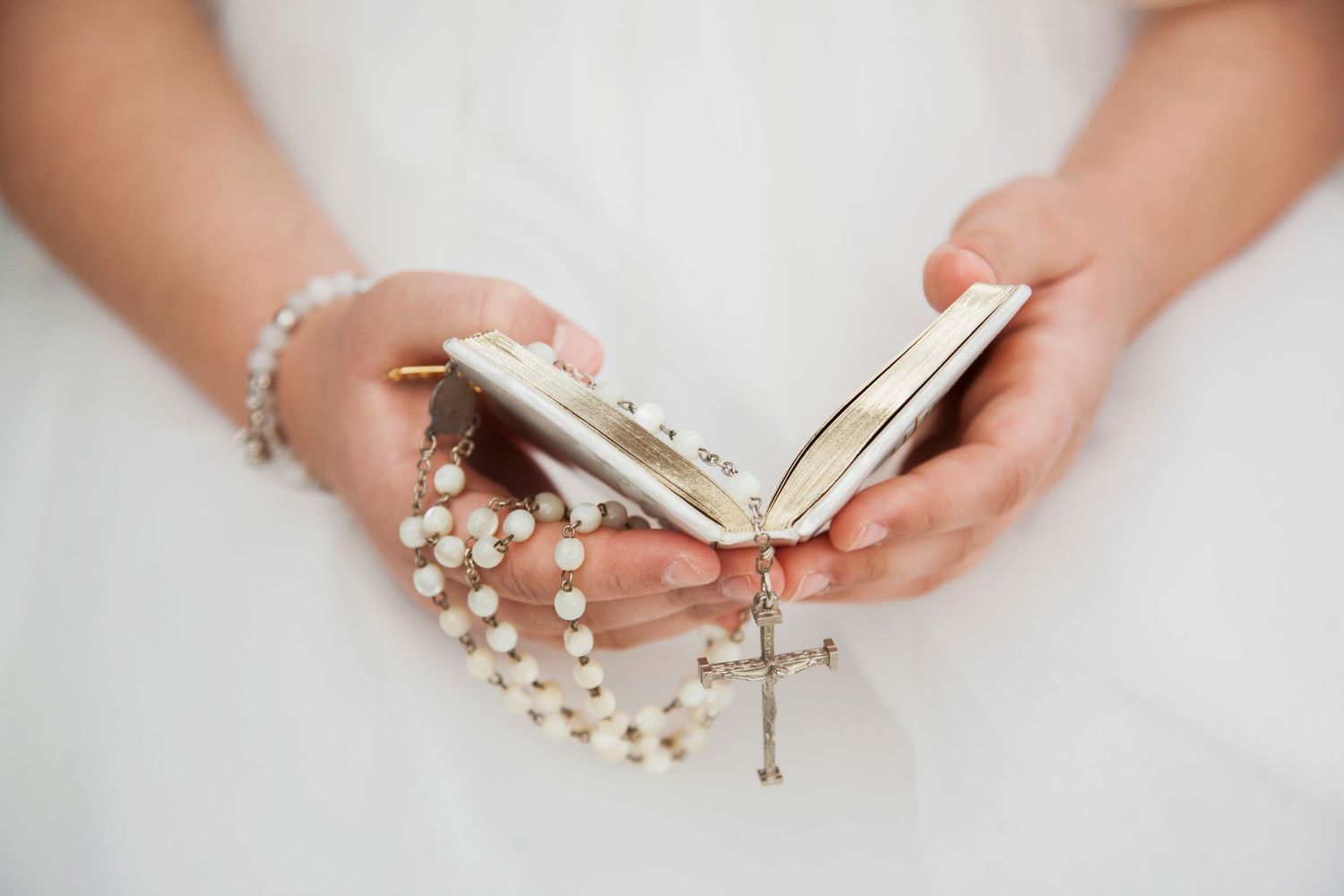Bride holding pearl rosary and small prayer book with cross pendant during wedding ceremony.