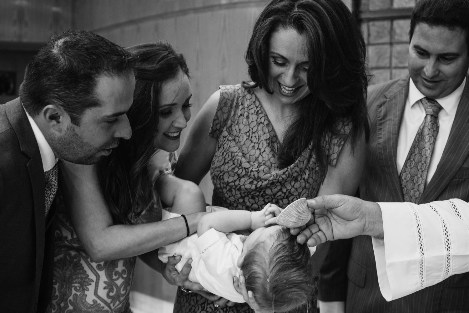 Black and white photo of family gathered around infant during baptism ceremony with priest.
