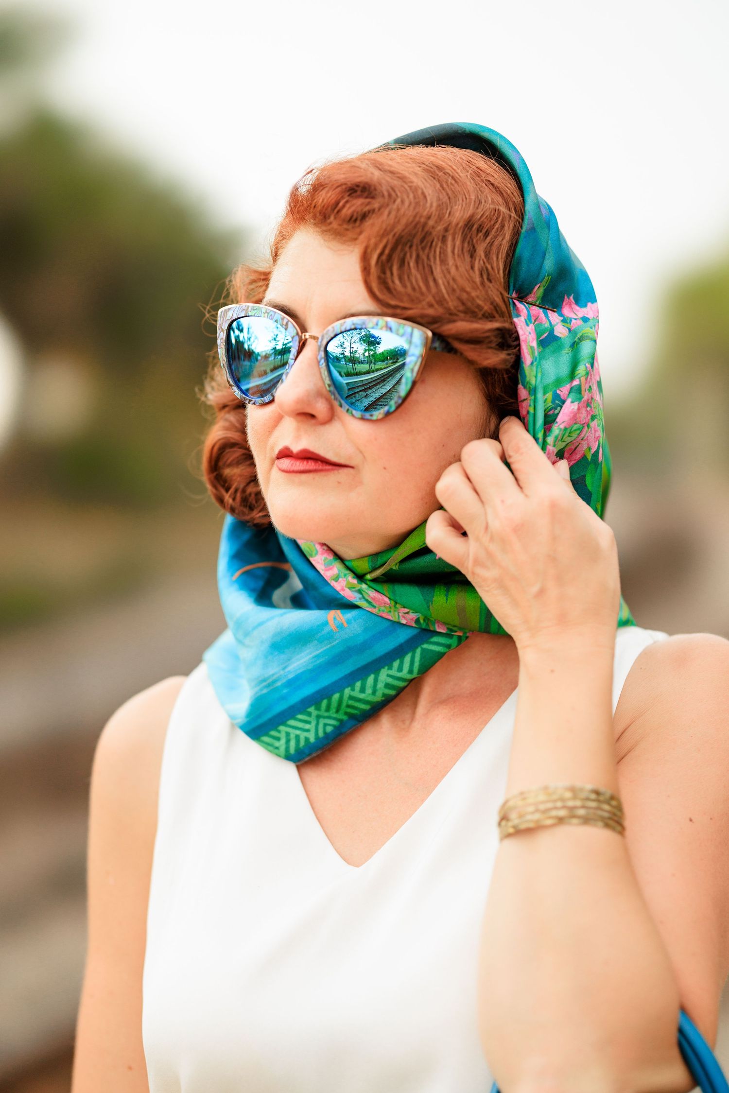 Woman in white top and teal headscarf wearing retro-style sunglasses.