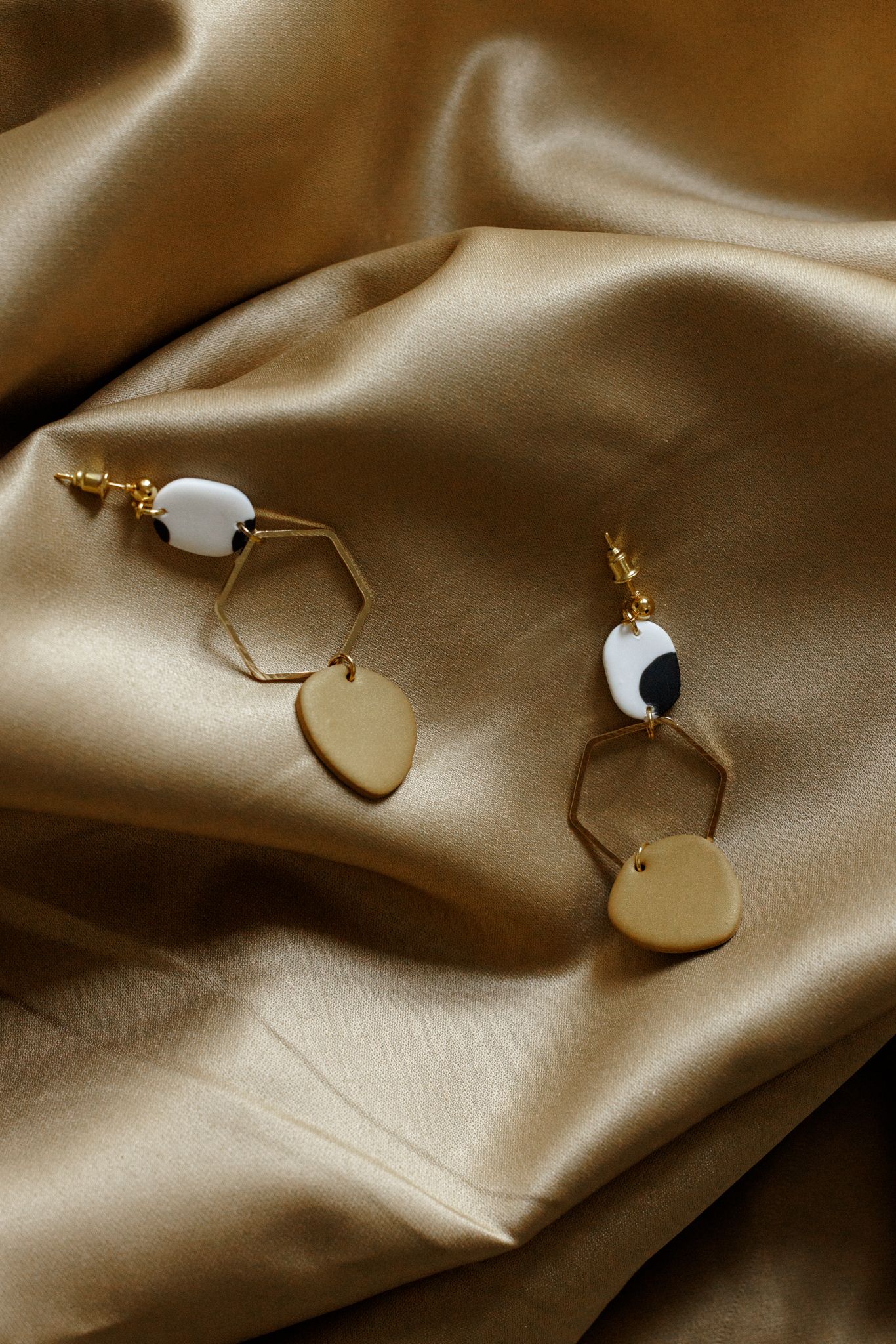 Minimalist gold disc earrings displayed on silky beige fabric.