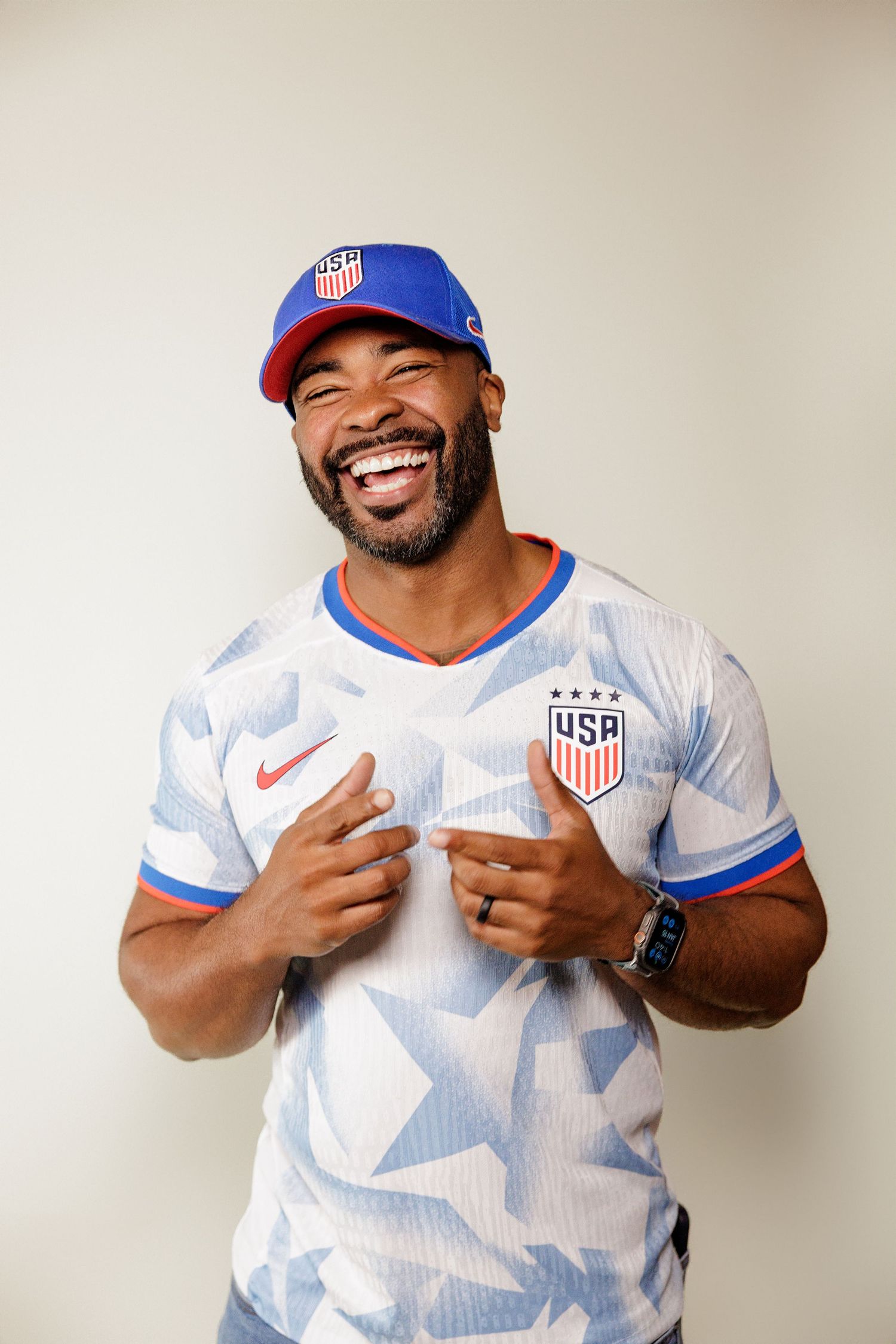 Soccer fan wearing USA national team jersey and blue cap poses expressively in studio photo series.