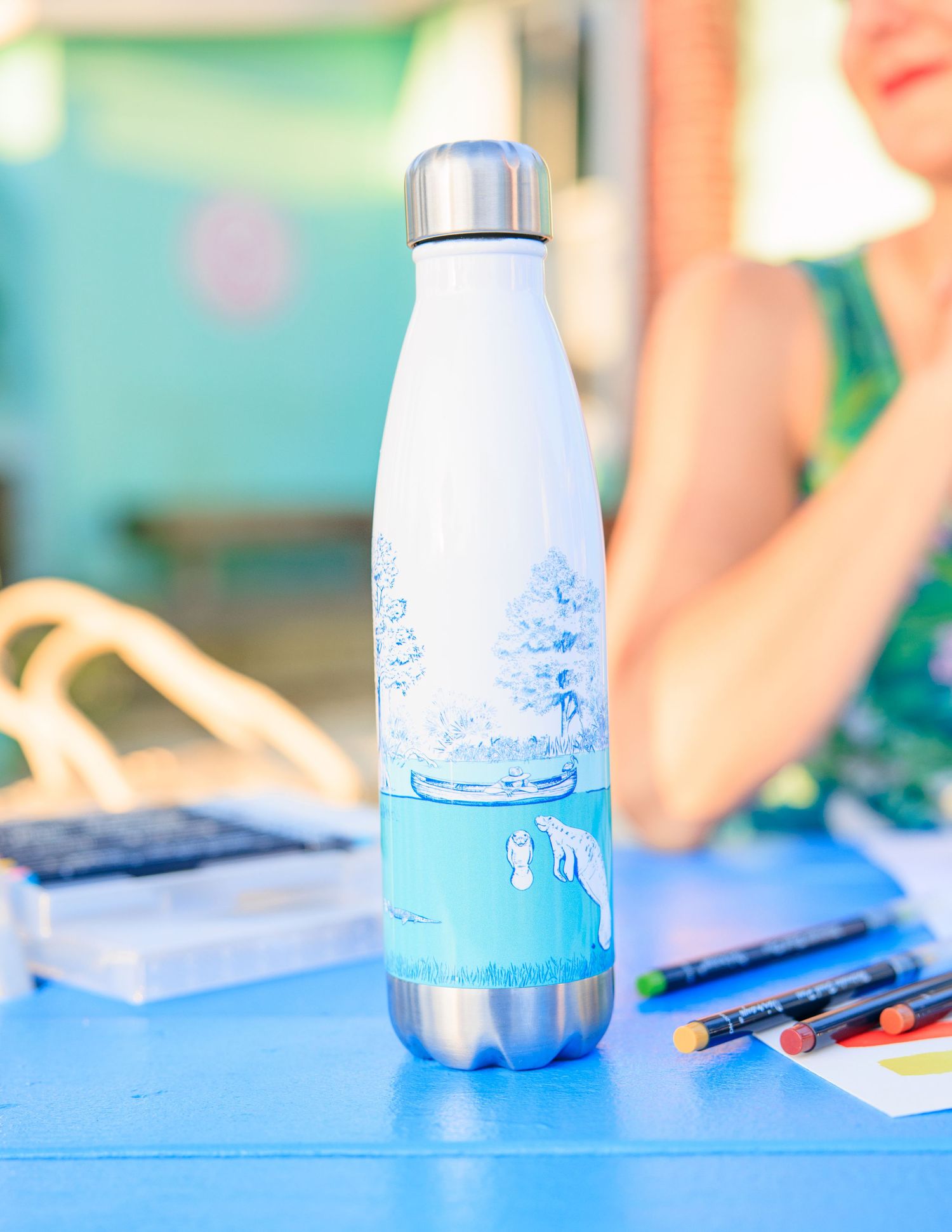 Blue water bottle and art supplies arranged on a bright surface for creative work.