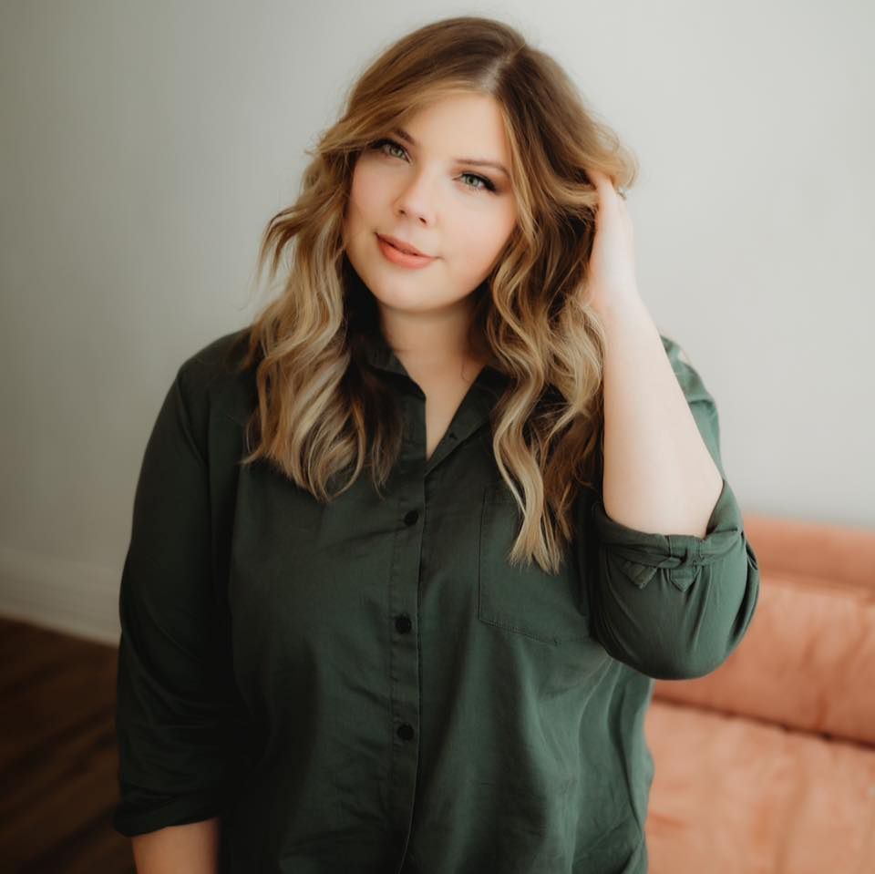 Portrait in an emerald green blouse with wavy blonde balayage hair against a neutral backdrop.