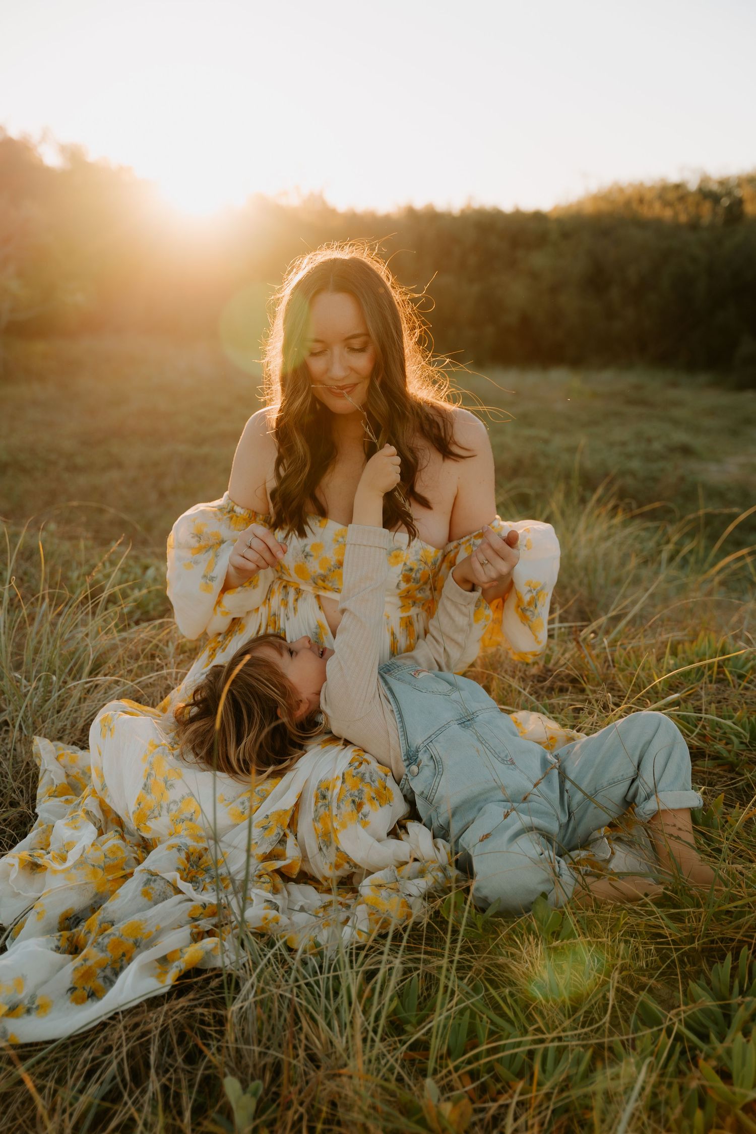 Mother and child in floral dress relaxing in sunlit meadow at golden hour.
