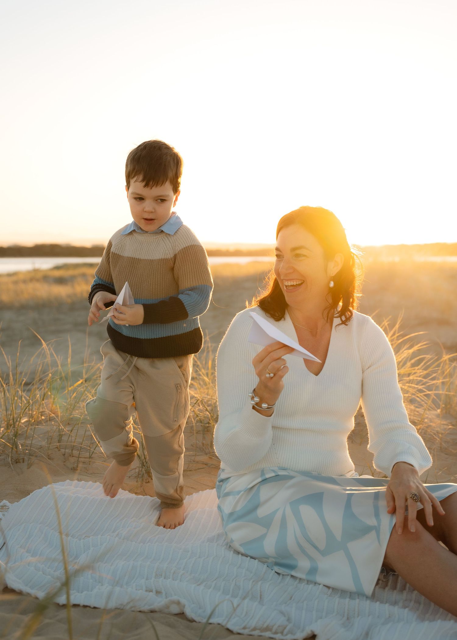A romantic couple sitting on a blanket at sunset with their small child in a peaceful outdoor setting.