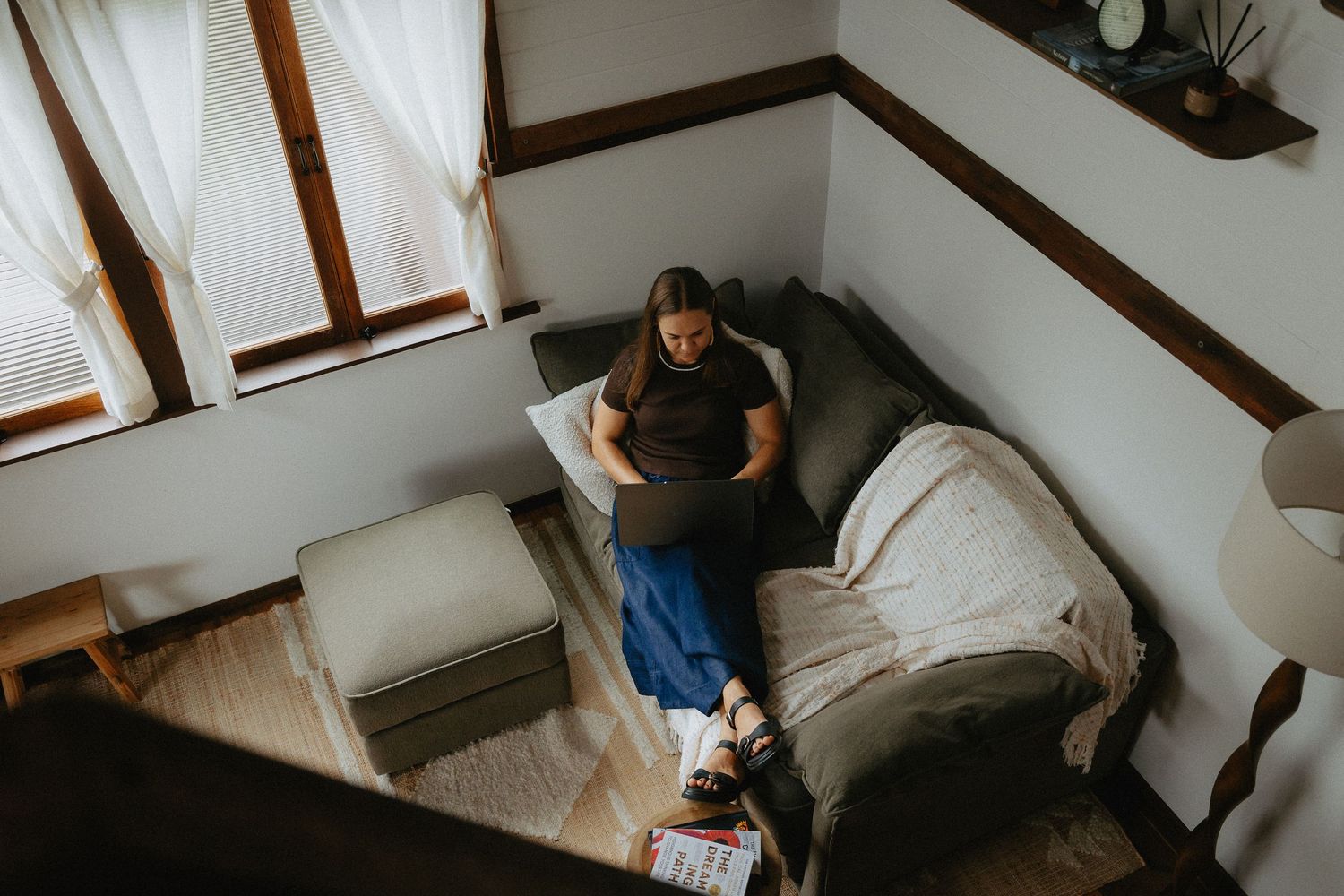 Overhead view of a pregnant woman sitting on a couch using a laptop in a cozy living room.