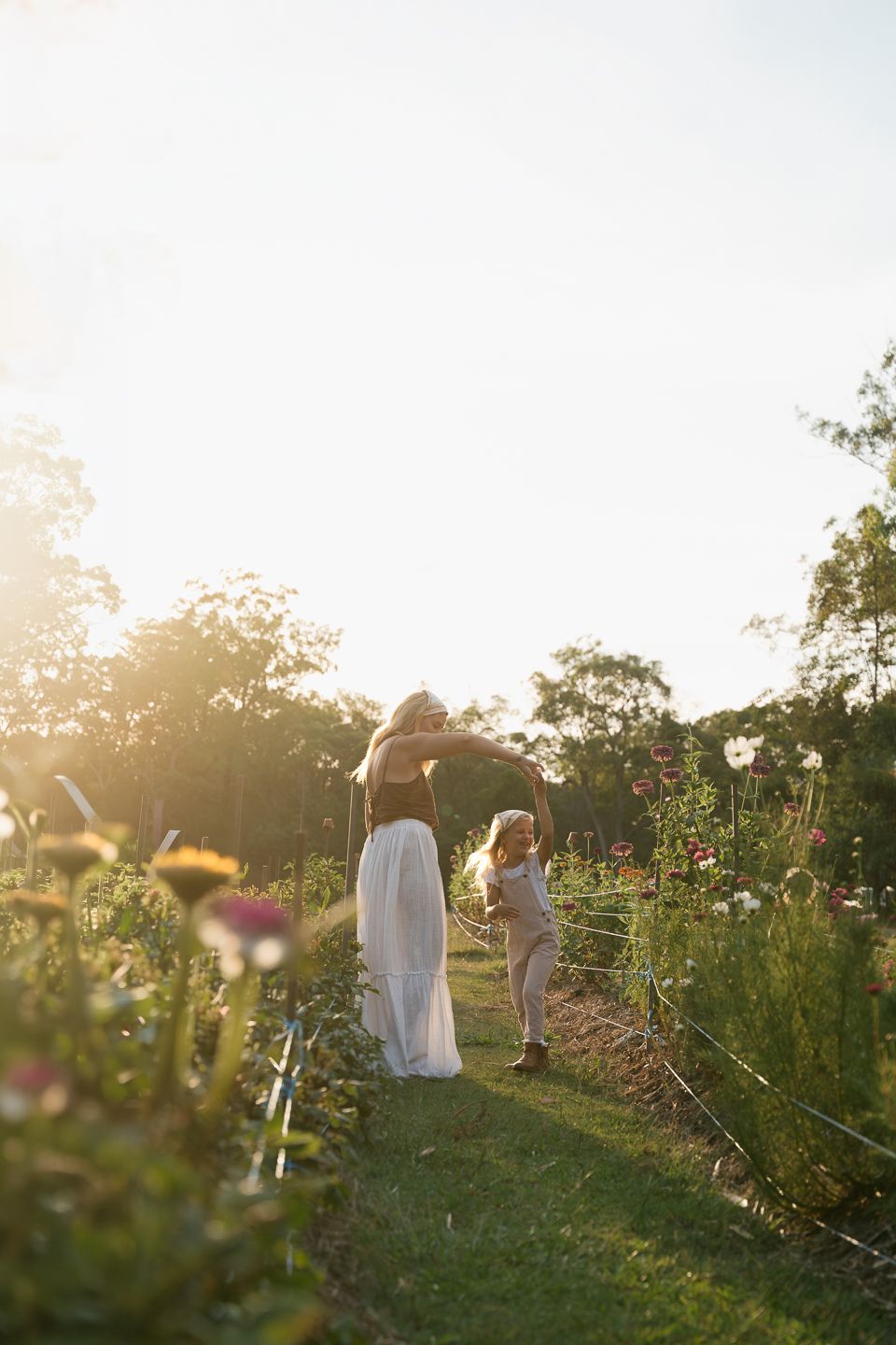 People walking through a sunlit garden with wildflowers at golden hour creating a dreamy summer atmosphere.