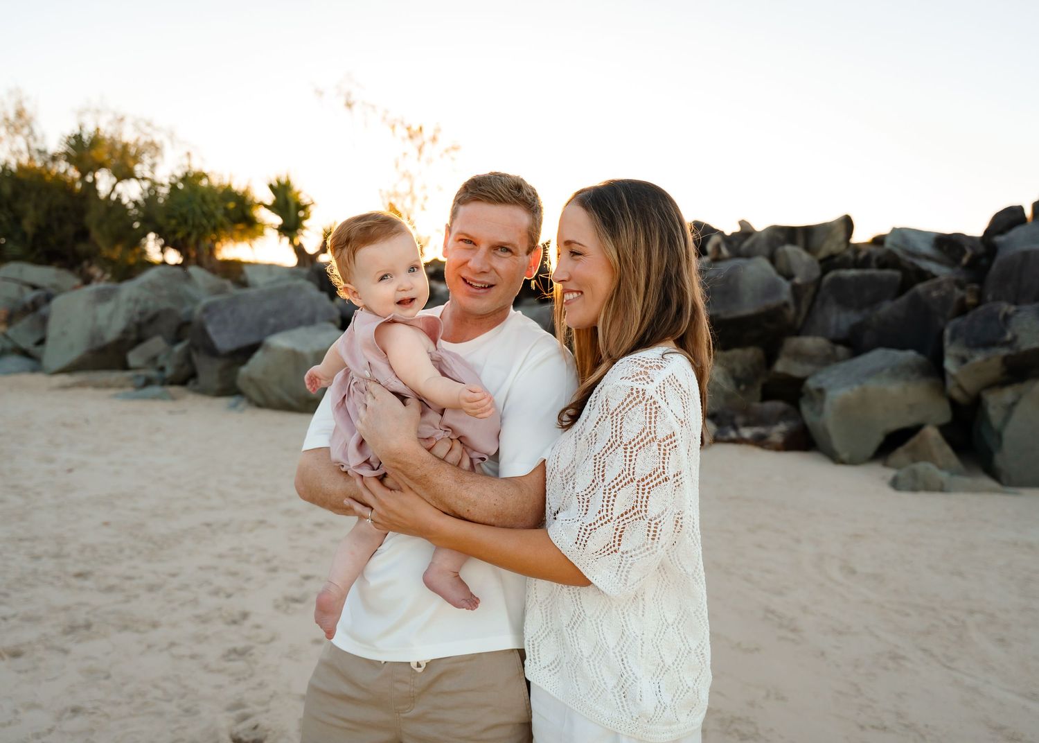 Happy family sharing tender moment together on beach with rocky backdrop at sunset.