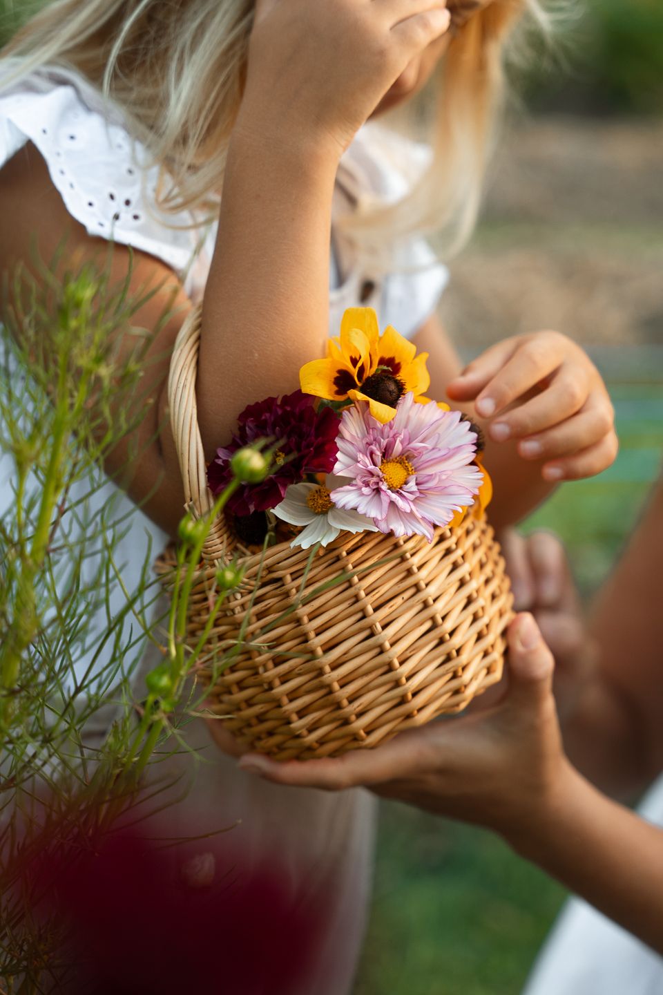 A woven basket being filled with colorful fresh flowers and greenery in a garden setting.