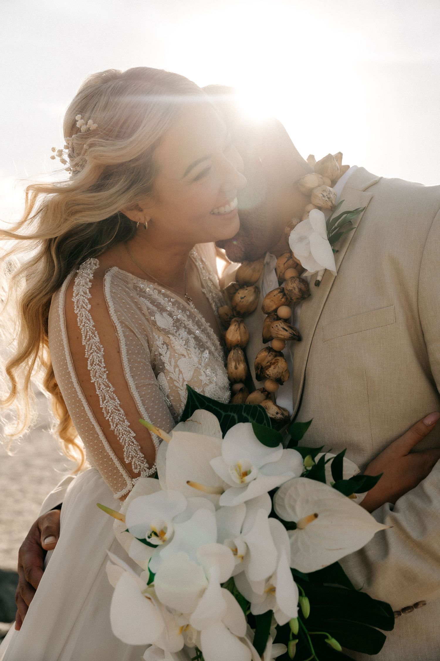 Bride and groom share a romantic moment at sunset beach wedding, bride holding white orchid bouquet.