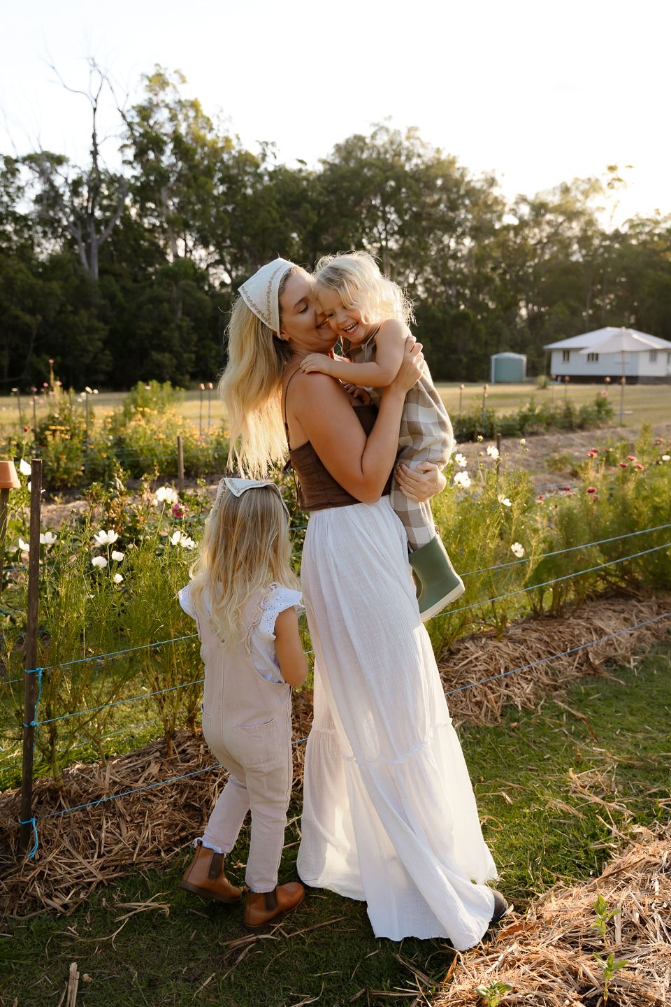 Two figures in white dresses explore a sunlit garden path together during golden hour.