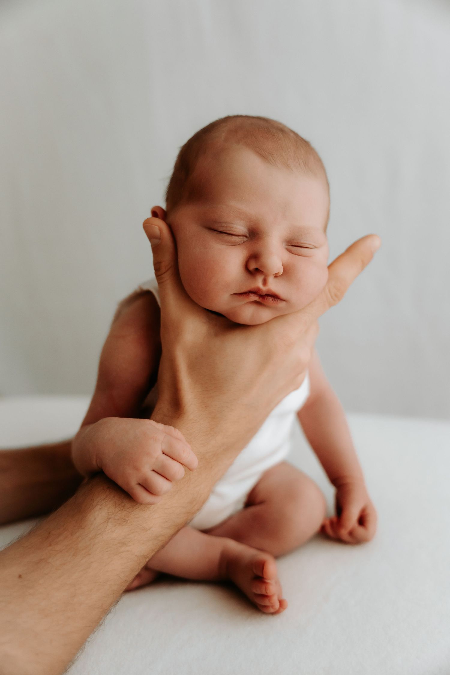 Peaceful sleeping newborn supported by adult hands against white background.
