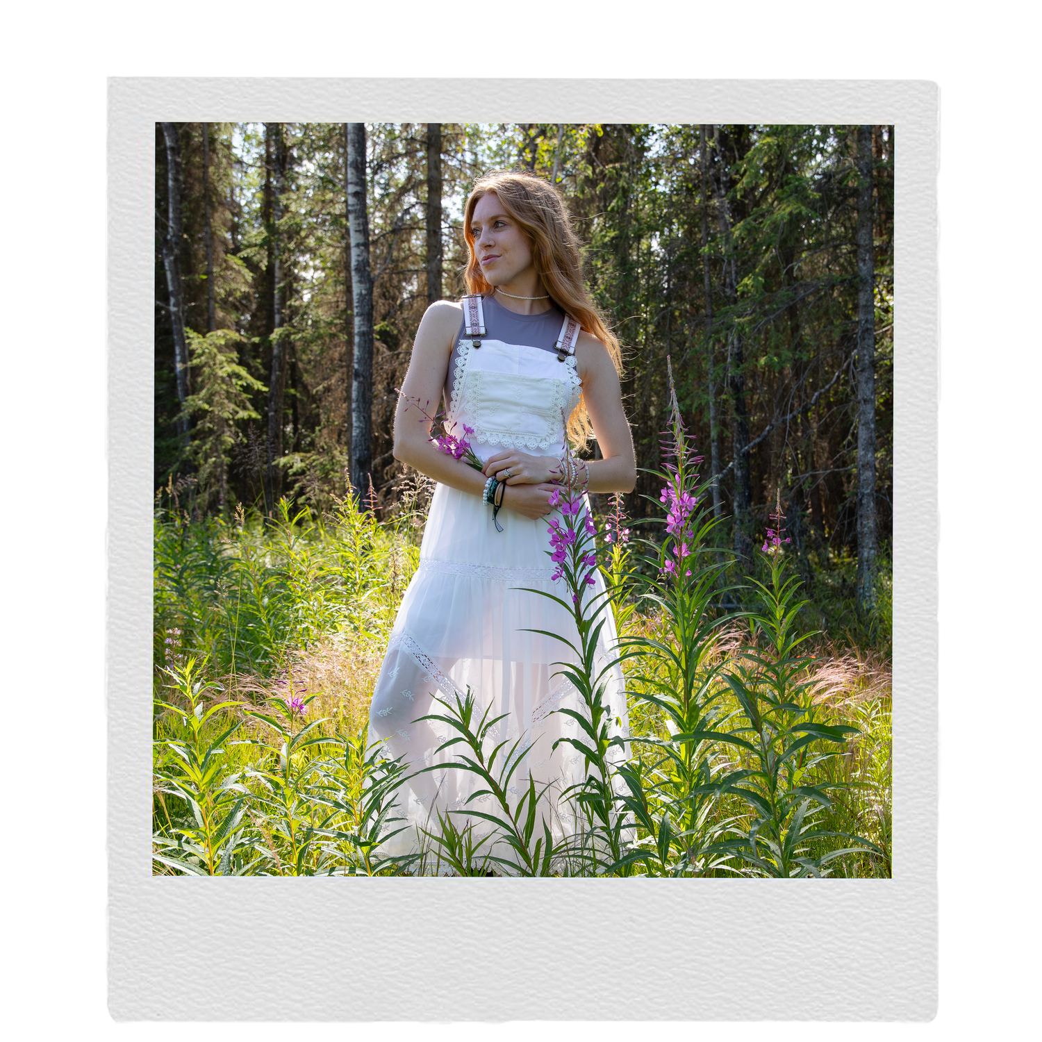 Woman in white dress standing among wildflowers in a sunlit forest clearing.
