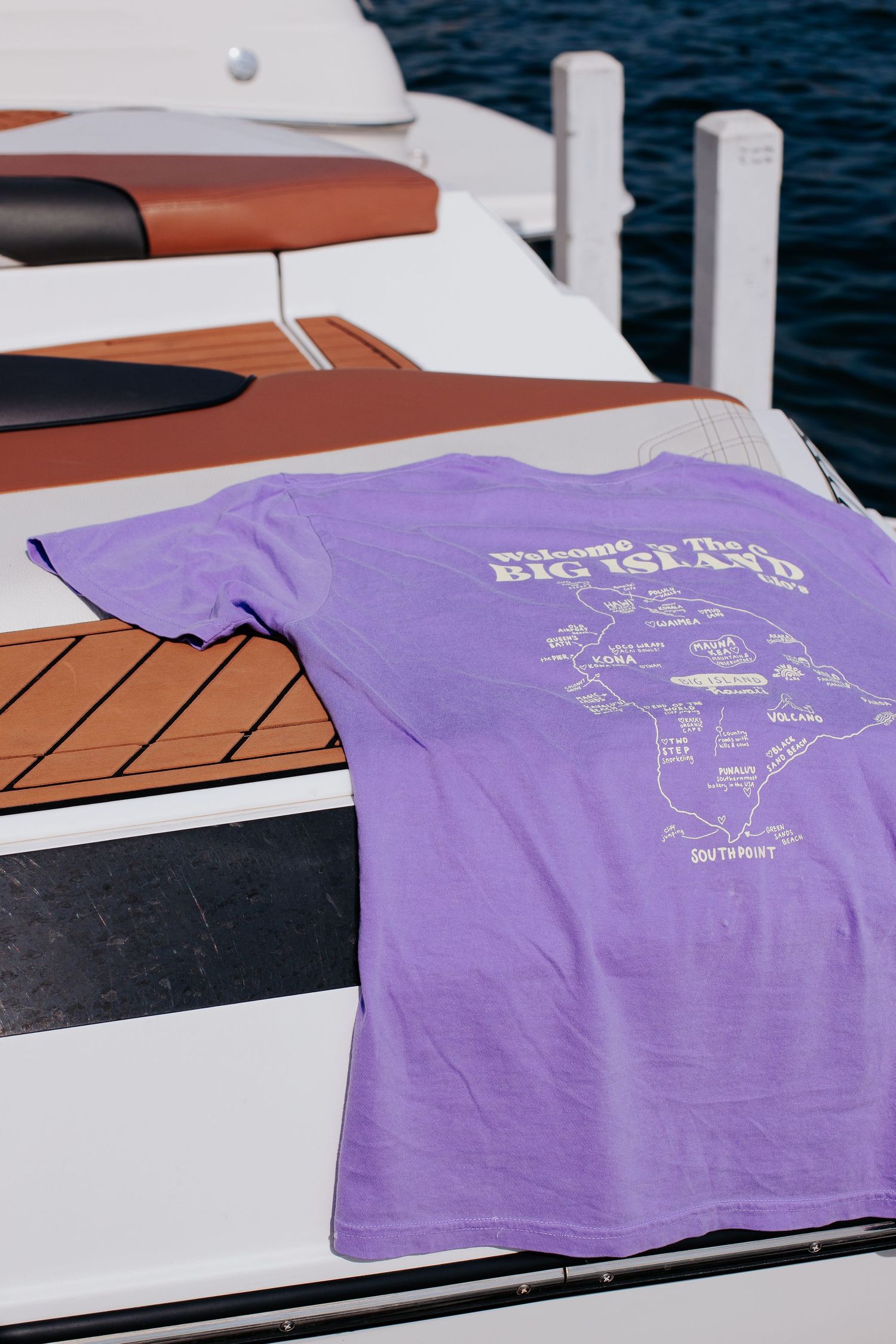 Purple t-shirt with graphic design laid flat on white boat deck.