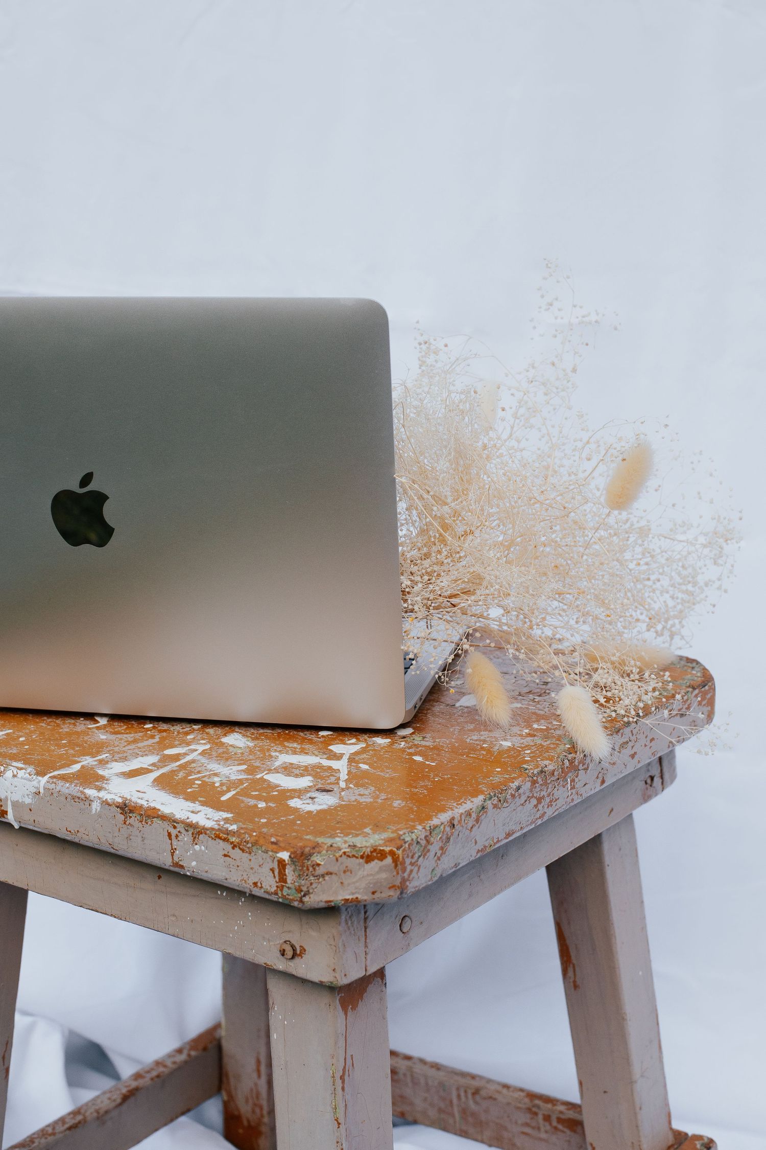 MacBook laptop sitting on a weathered rustic wooden stool against white background.