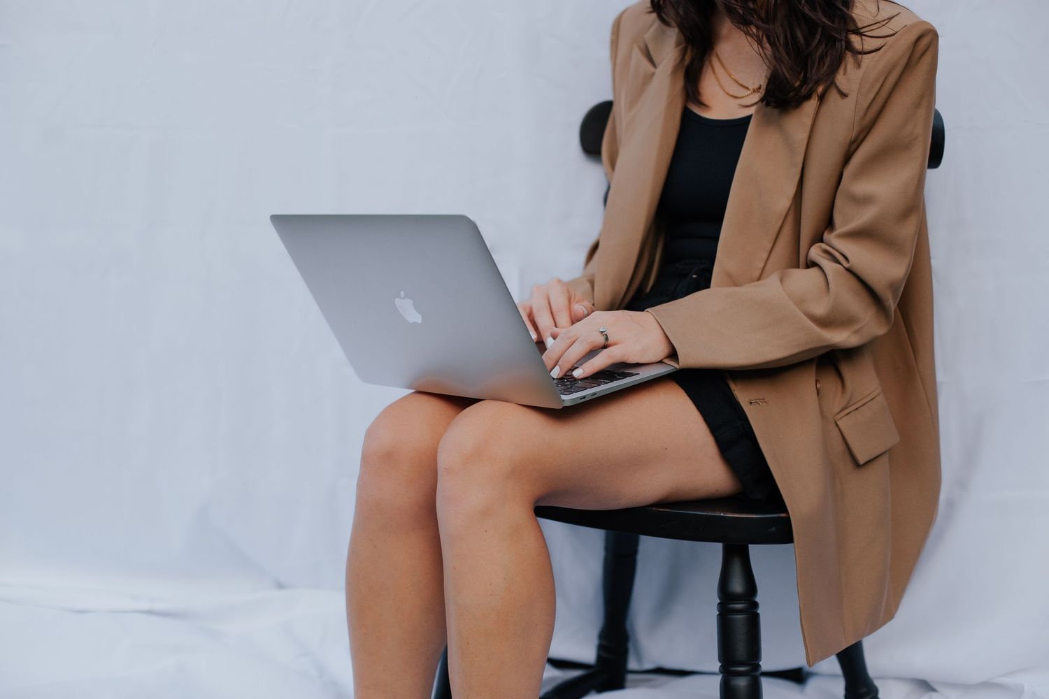 Professional photo session featuring tan blazer and laptop on wooden stool.