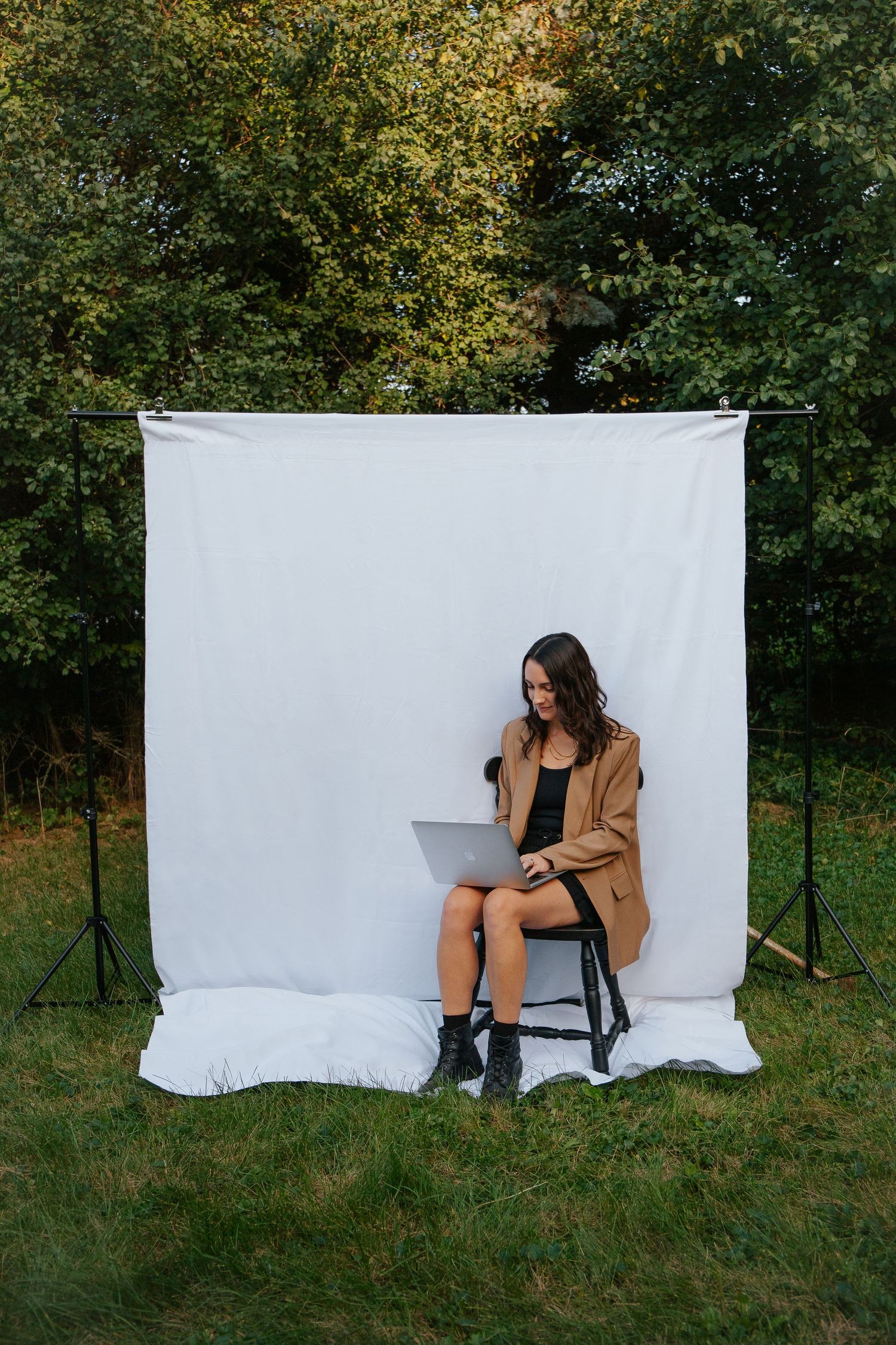 Lifestyle photoshoot outdoors with white backdrop and chair setup in a grassy field with autumn trees.