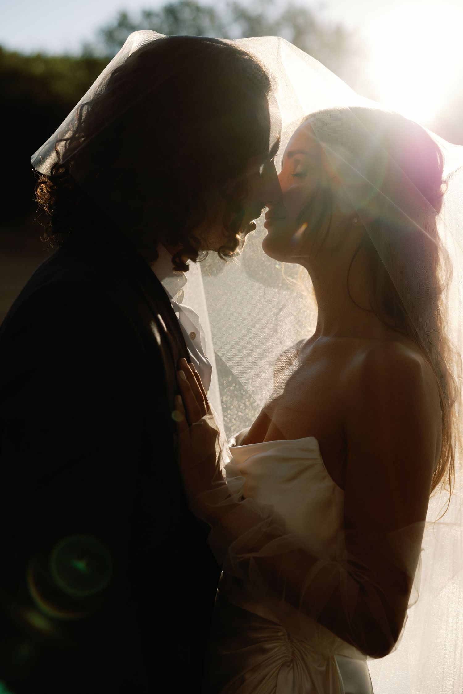 A romantic silhouette of a bride and groom sharing an intimate moment in golden sunlight with lens flare.