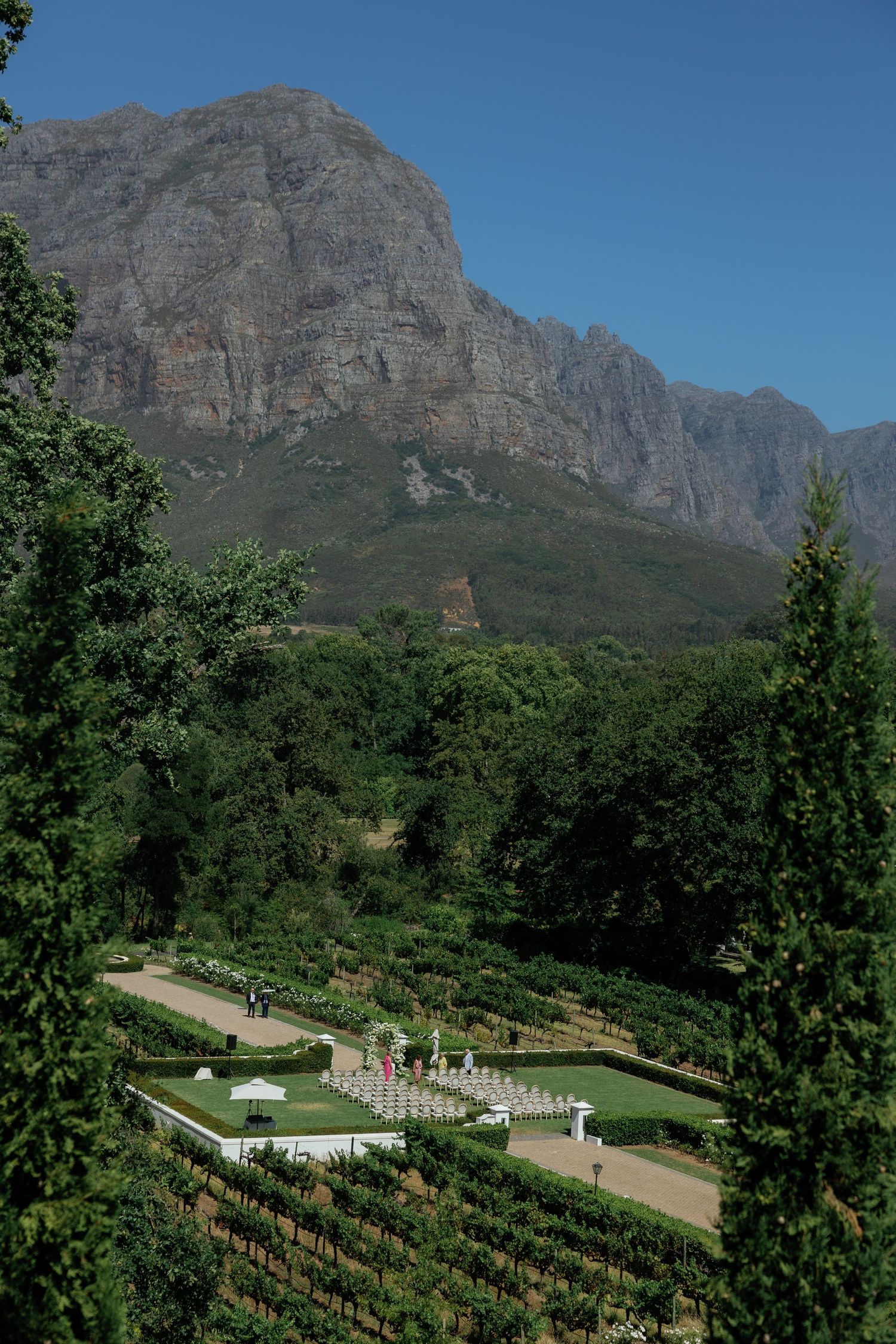 Panoramic view of a terraced garden nestled against majestic mountain peaks with lush greenery and winding pathways.
