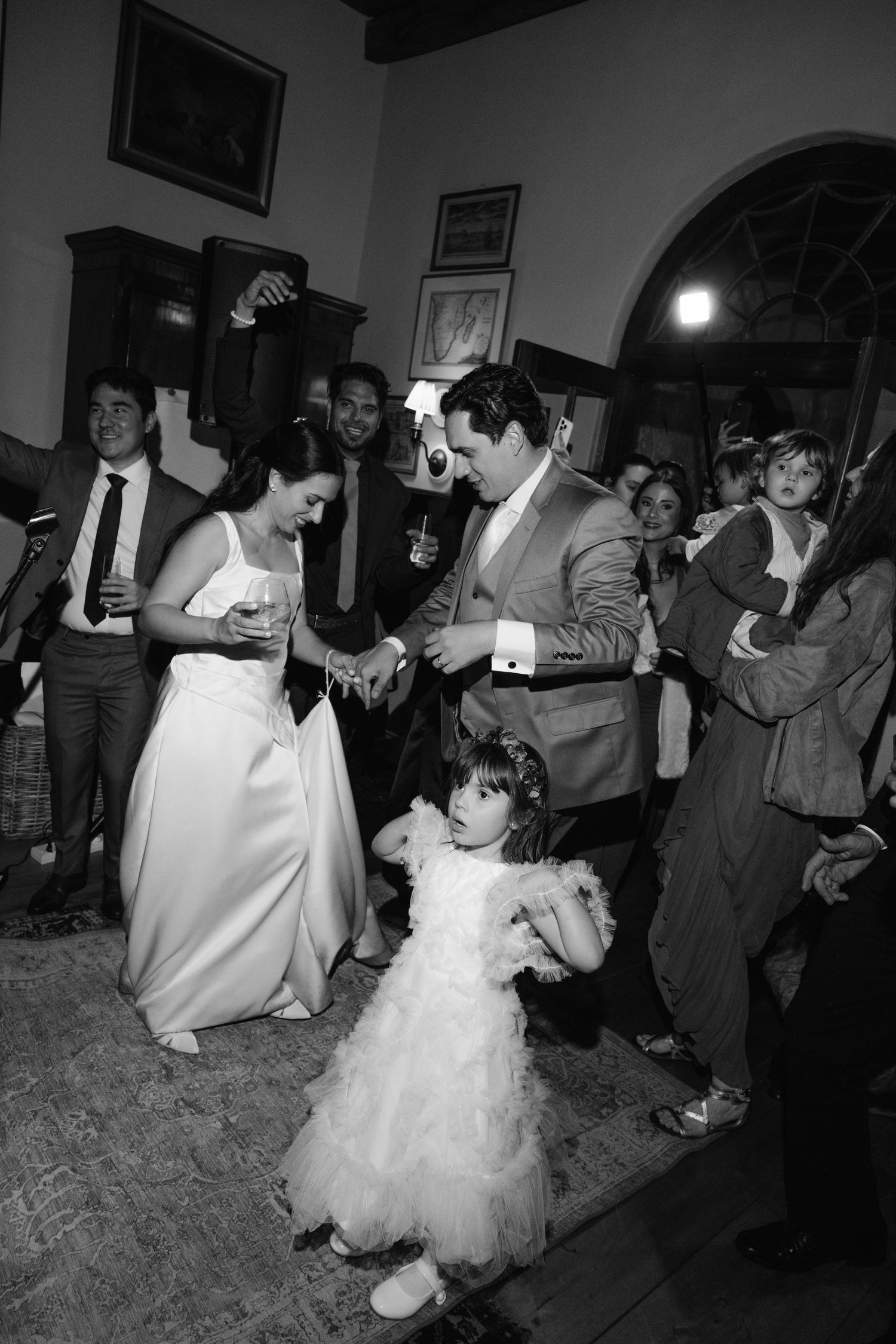Black and white photo of bride and groom dancing with flower girl at wedding reception.